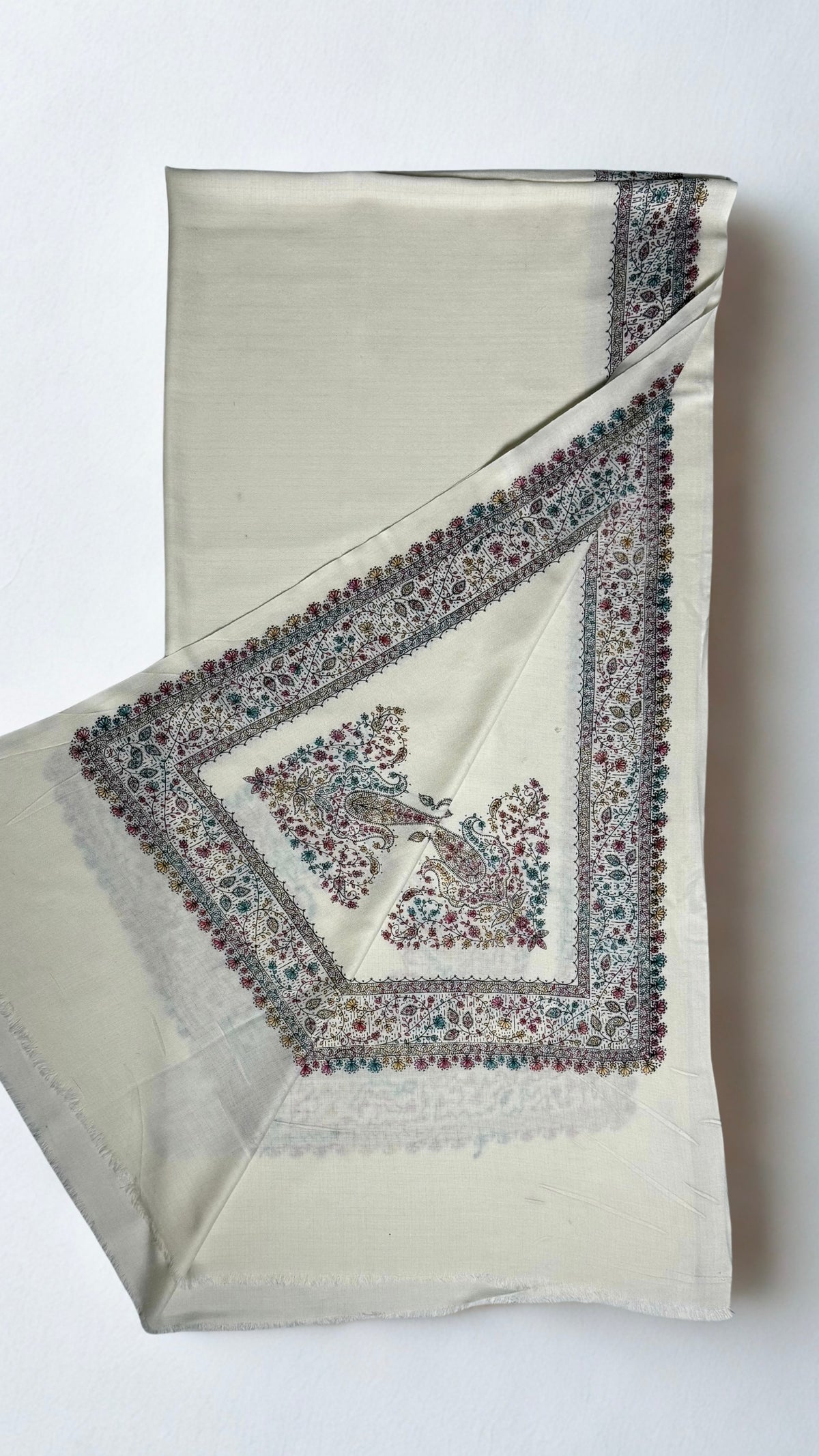 White Swati Shahtoosh shawl with one corner turned back, showing the deep hand-embroidered border mitred at the corner around a pair of paisley motifs