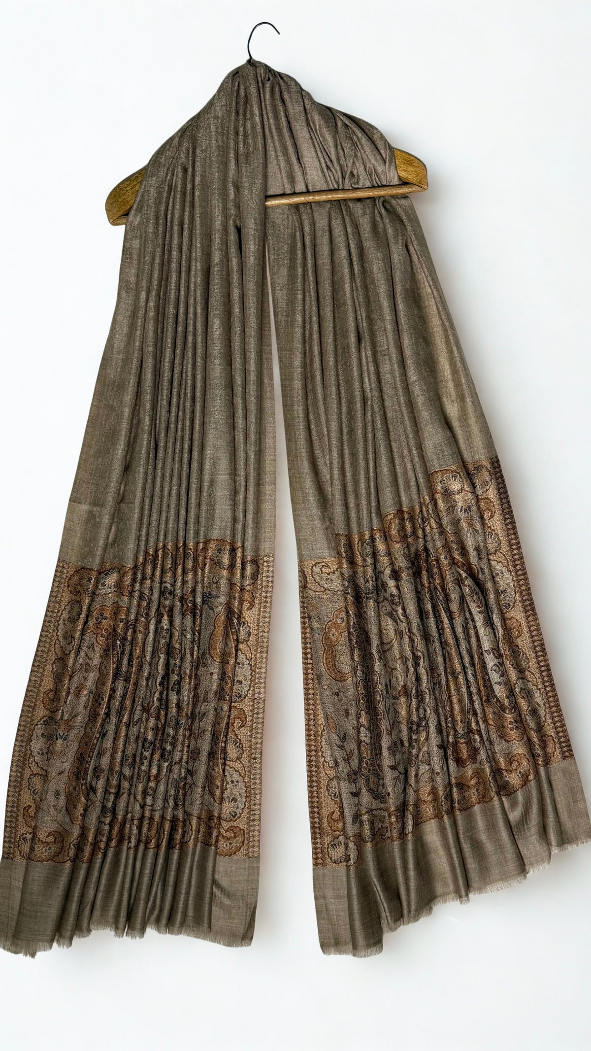 Warm khaki fine pashmina ring shawl hanging from a wooden hanger, with woven copper paisley pallas at both ends