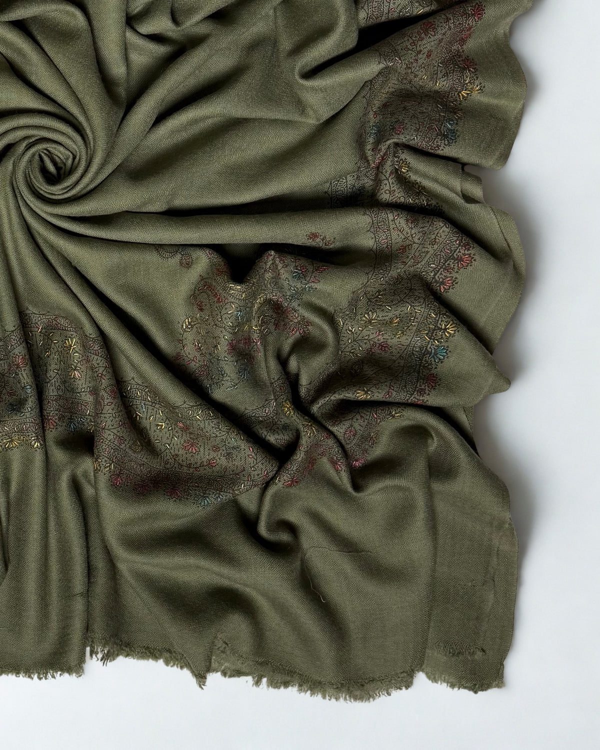 Close-up of the hand-embroidered floral vine border and fringed edge on the olive green Swati Shahtoosh shawl