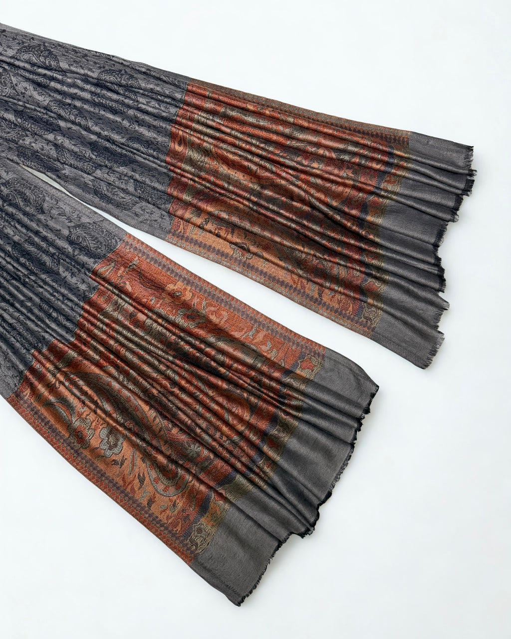 Both ends of a charcoal pashmina ring shawl laid out, showing the woven rust and copper paisley pallas against the dark patterned field