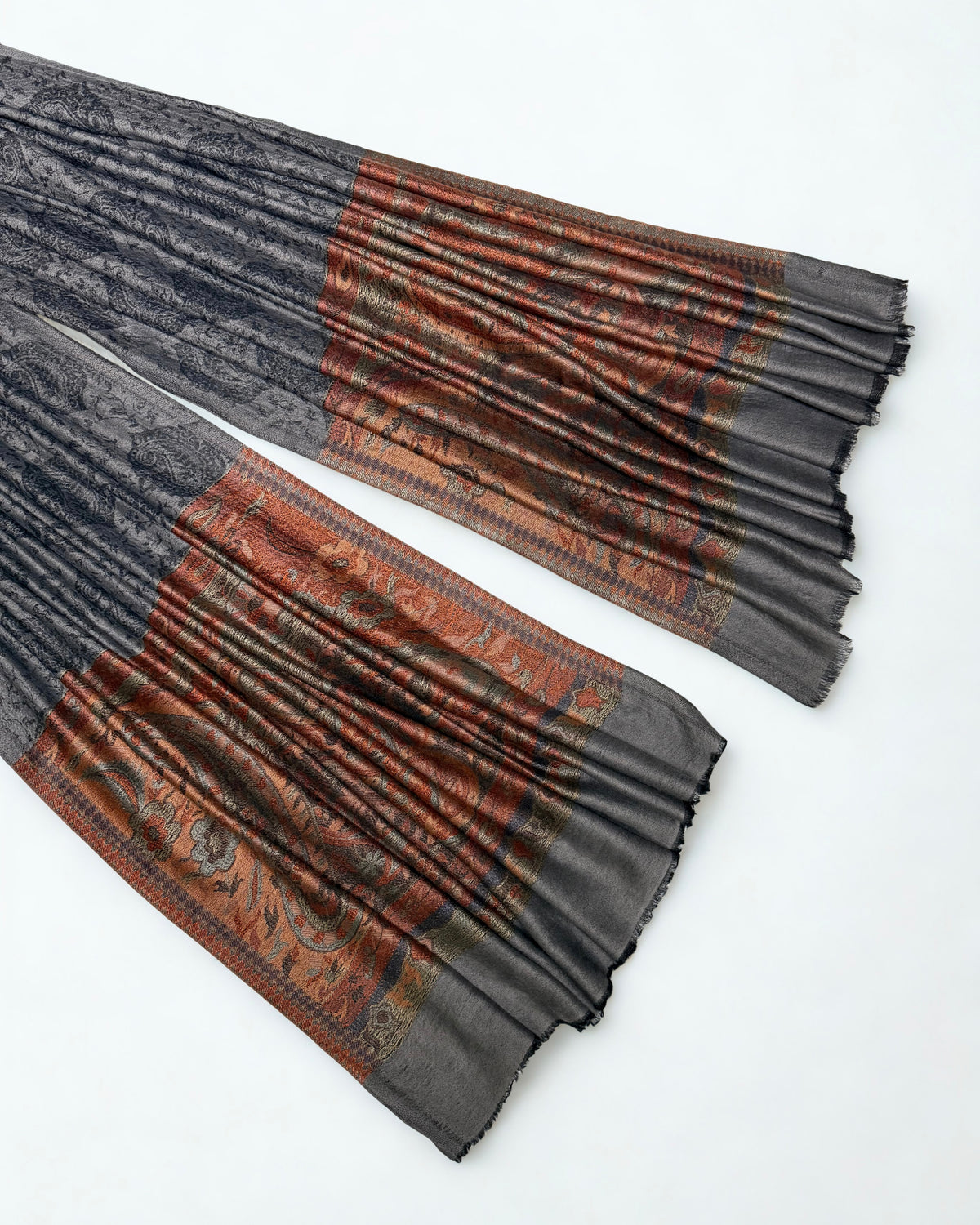 Both ends of a charcoal pashmina ring shawl laid out, showing the woven rust and copper paisley pallas against the dark patterned field