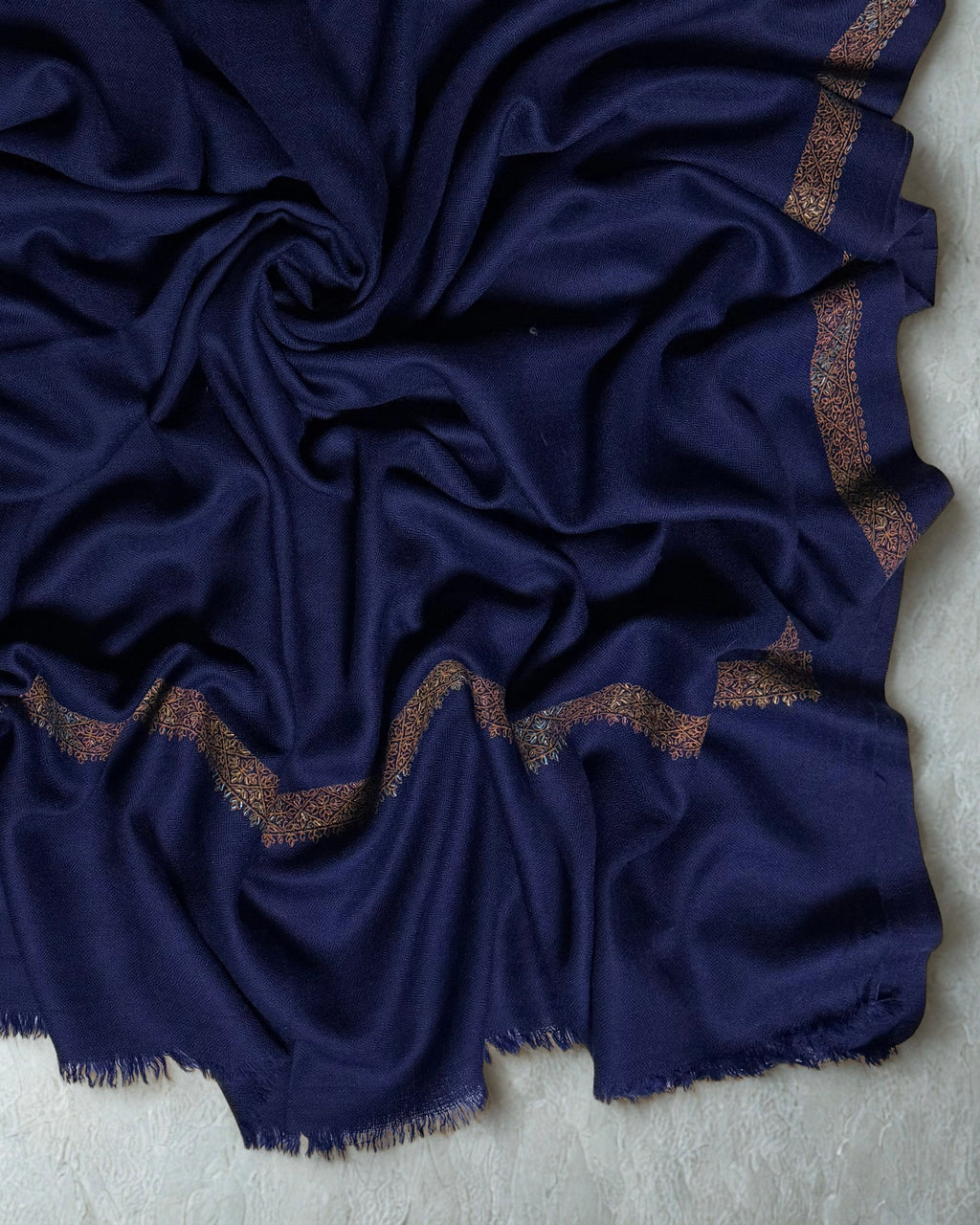 Close-up of the scalloped hand-embroidered gold border and fringed edge on the navy Swati Shahtoosh shawl