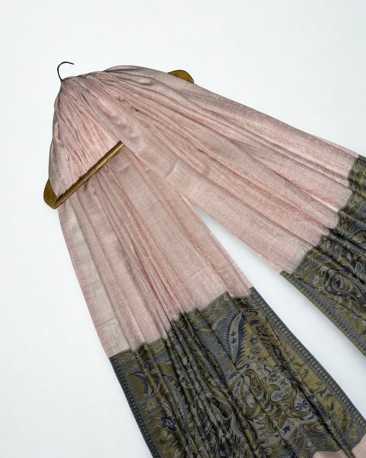 Blush pink Palladar ring shawl hanging from a wooden hanger, seen at an angle, with the dark paisley pallas falling at both ends