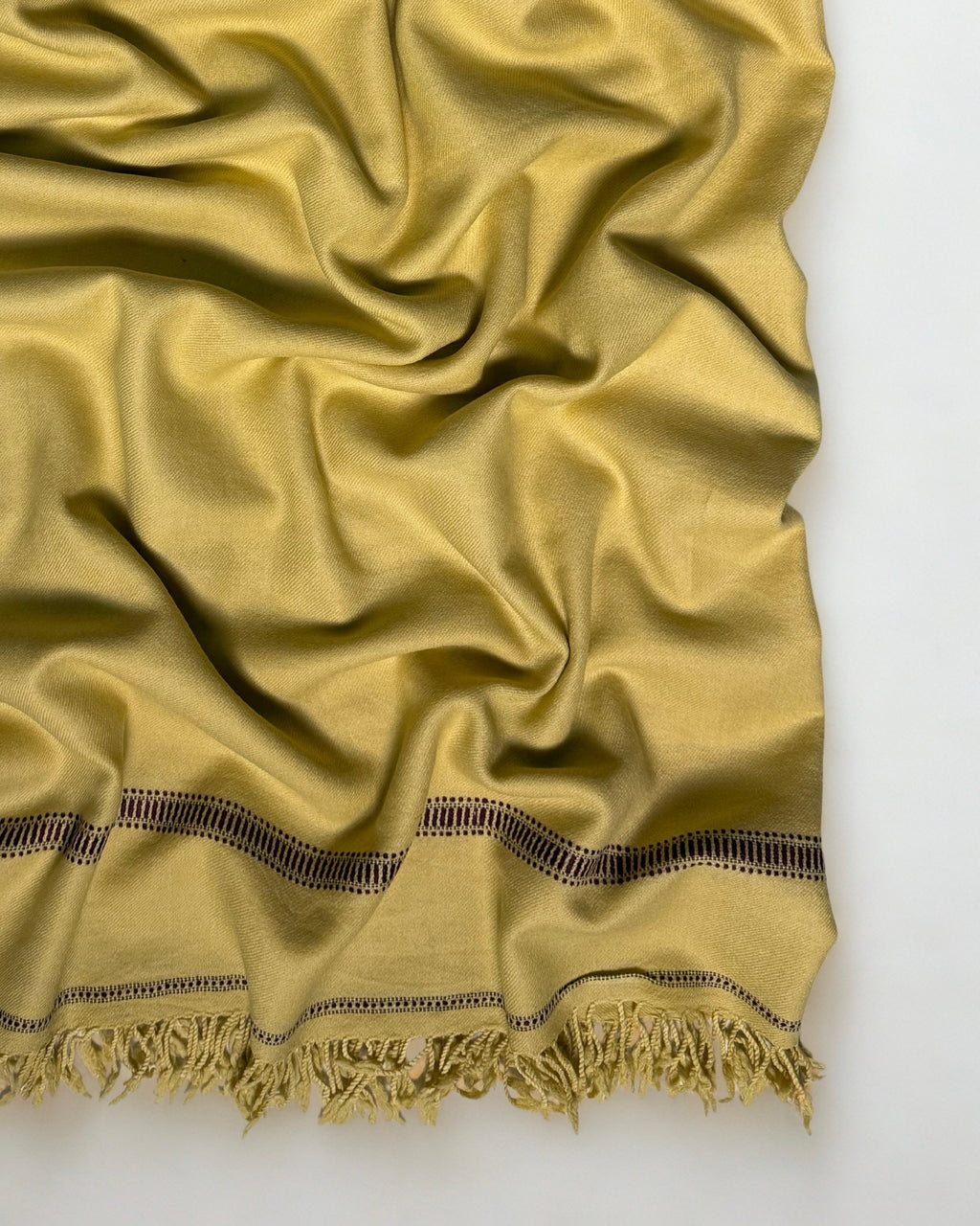 Close-up of the olive gold men's Swati pashmina shawl showing the woven openwork band and knotted fringe