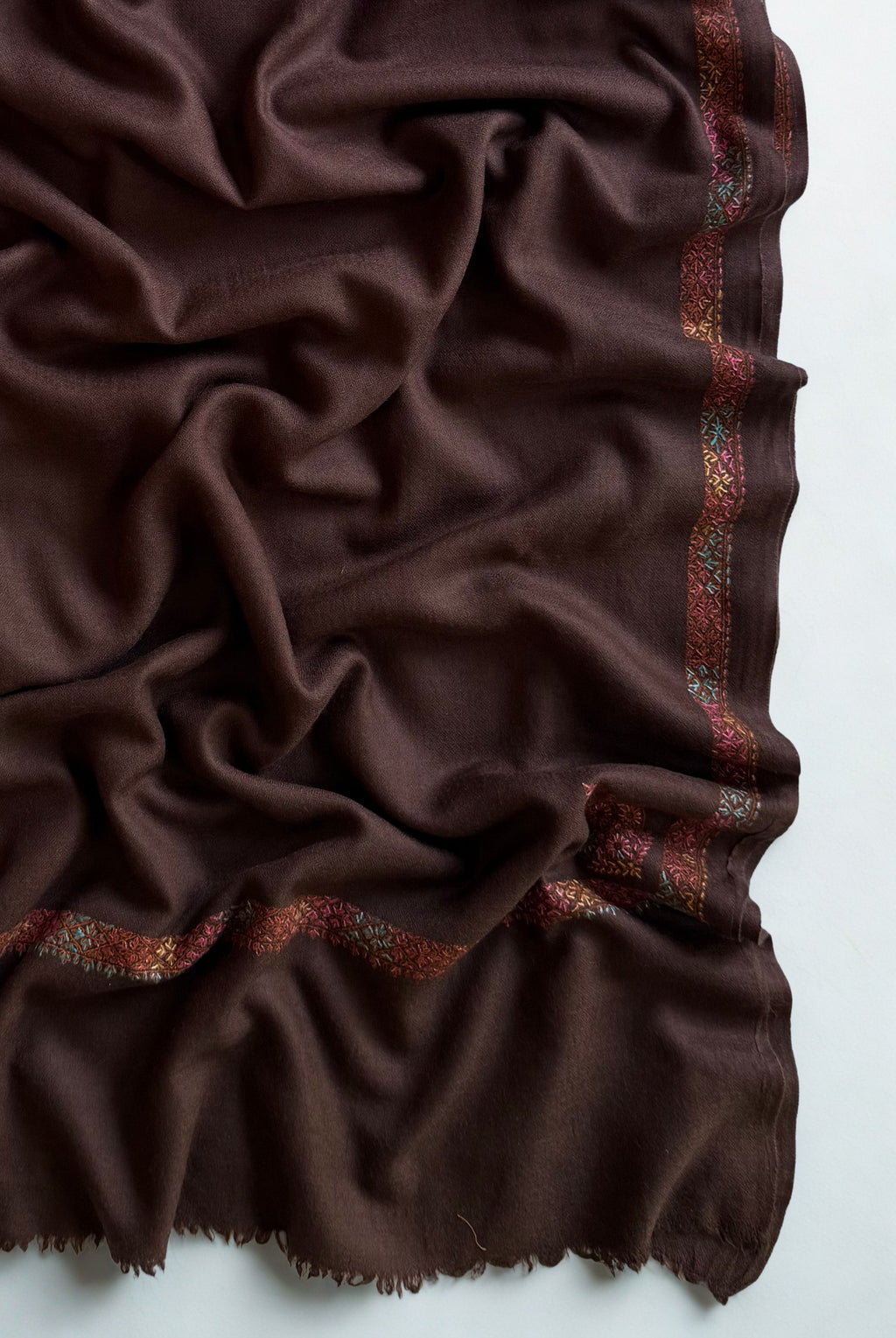 Espresso brown Swati Shahtoosh shawl folded in layers, showing the border running along the edge and the fringed end