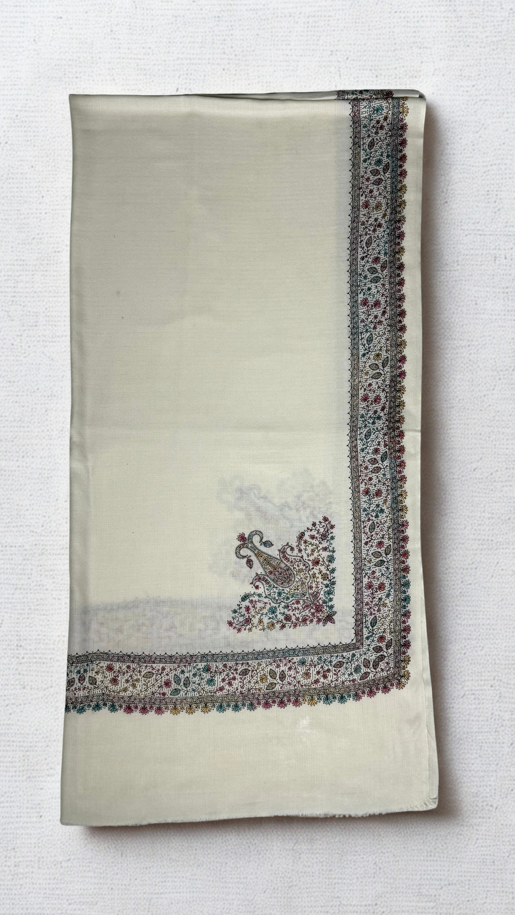 Ivory white Swati Shahtoosh shawl folded lengthwise, with a wide hand-embroidered paisley border in rose, teal and gold running down the edge and a large paisley motif at the corner
