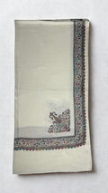 Ivory white Swati Shahtoosh shawl folded lengthwise, with a wide hand-embroidered paisley border in rose, teal and gold running down the edge and a large paisley motif at the corner