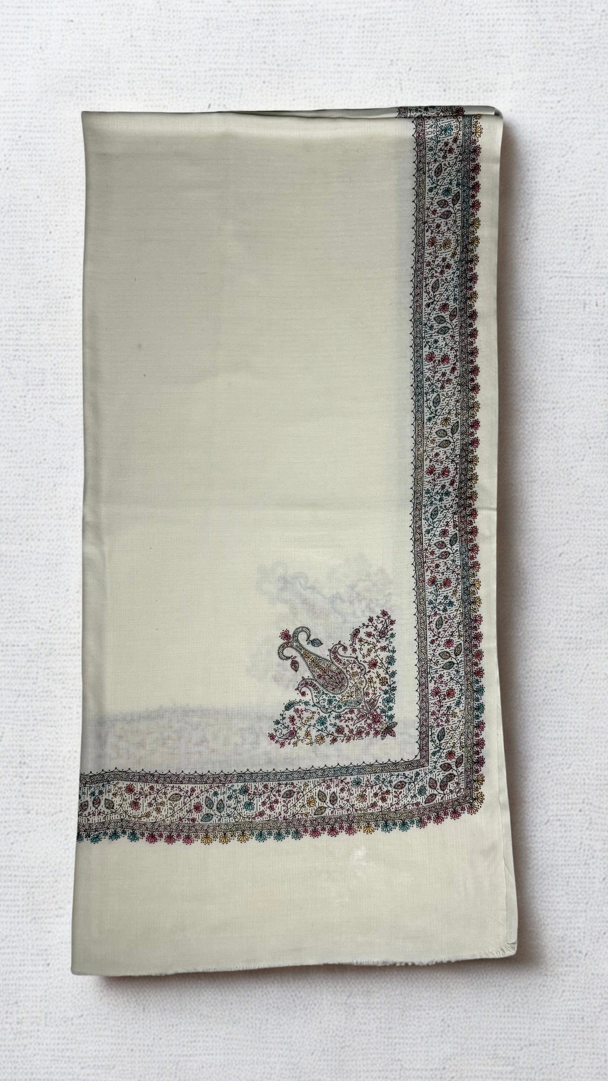 Ivory white Swati Shahtoosh shawl folded lengthwise, with a wide hand-embroidered paisley border in rose, teal and gold running down the edge and a large paisley motif at the corner