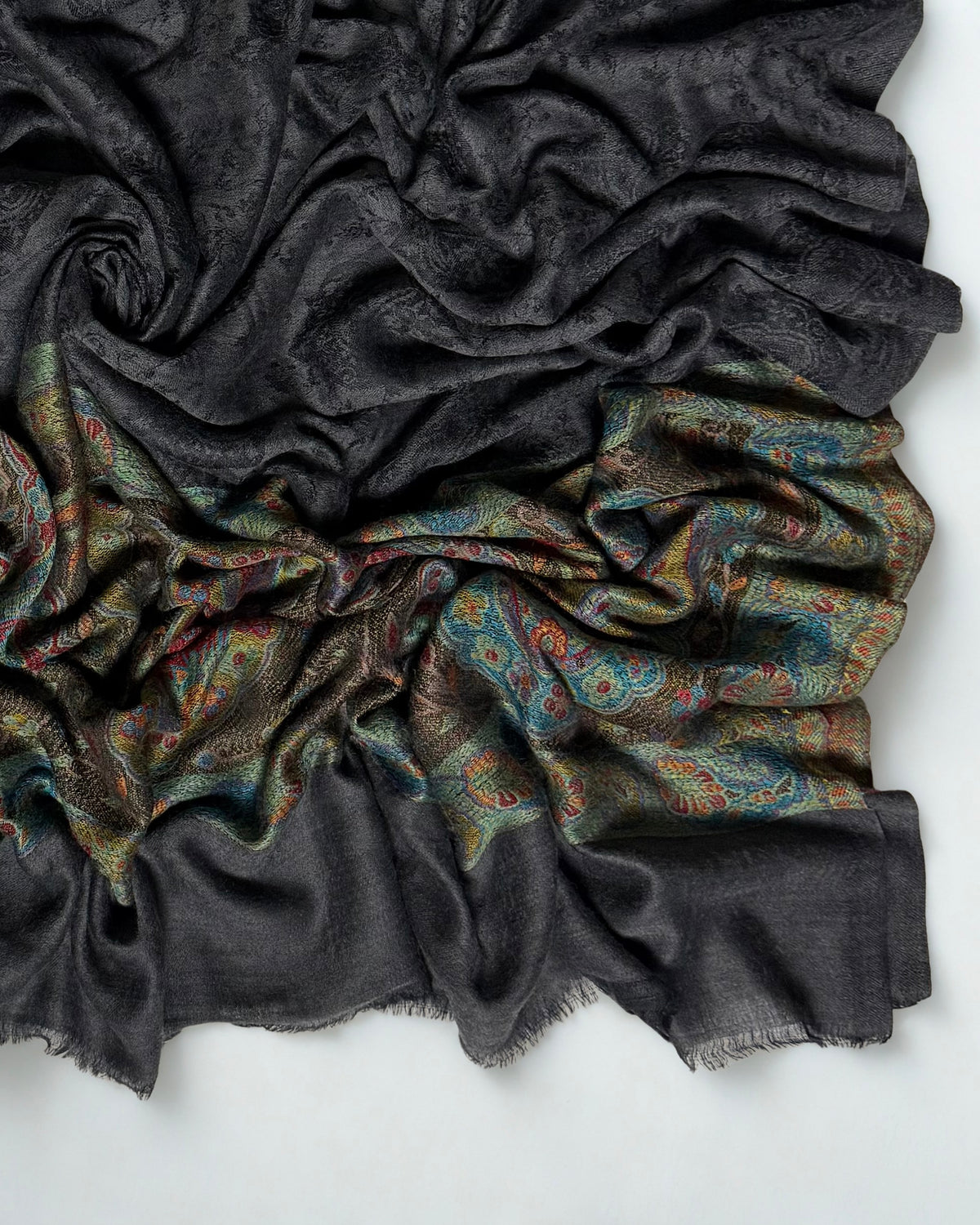 Close-up of a dark charcoal Palladar shawl swirled to show the jewel-tone paisley palla and plain fringed end