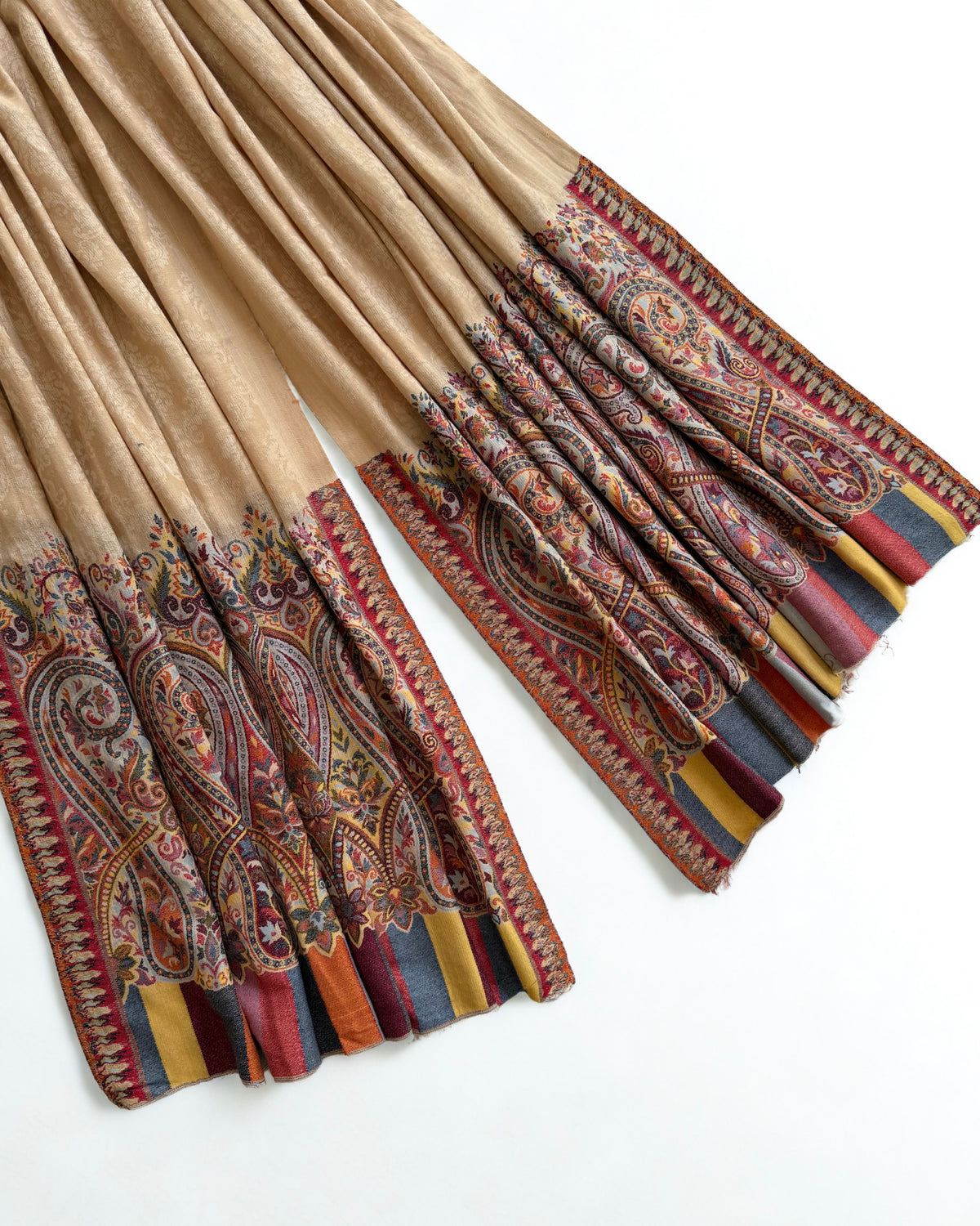Sand pashmina shawl swirled to show its drape and the paisley border beneath
