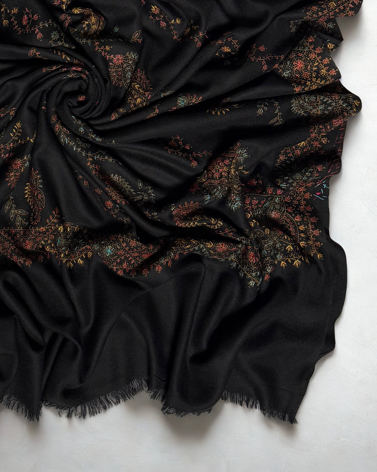Close-up of a black Swati Shahtoosh shawl swirled to show multicolour hand embroidery and the soft plain black fringed end