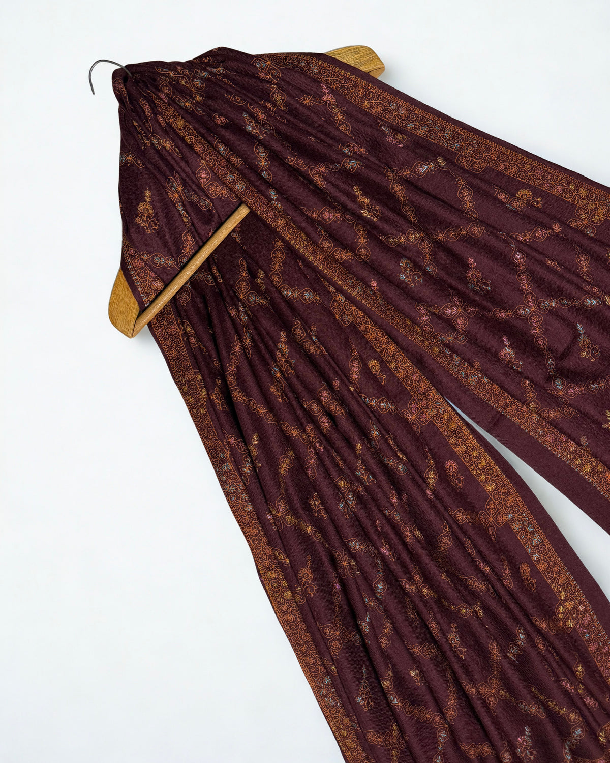 Wine Swati Shahtoosh shawl draped over a wooden hanger, embroidery running through the folds
