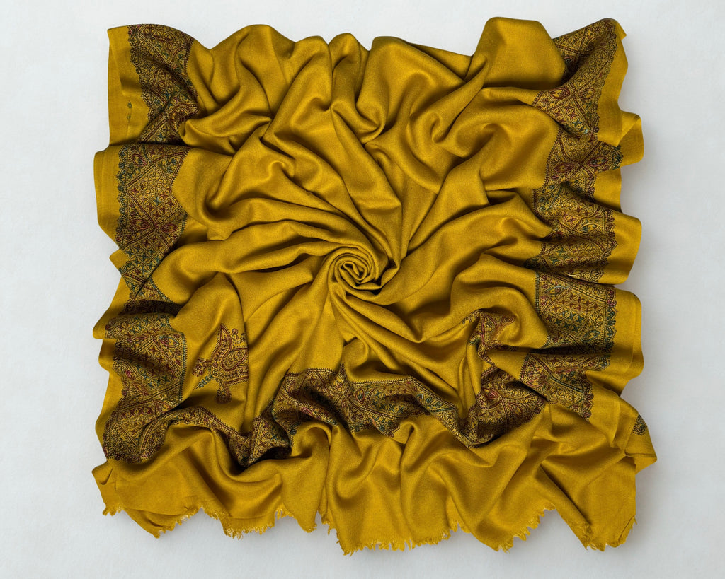 Full view of the mustard gold Swati Shahtoosh shawl gathered in a swirl, the hand-embroidered lattice border framing all four sides