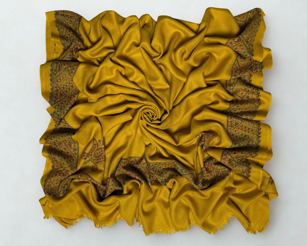 Full view of the mustard gold Swati Shahtoosh shawl gathered in a swirl, the hand-embroidered lattice border framing all four sides
