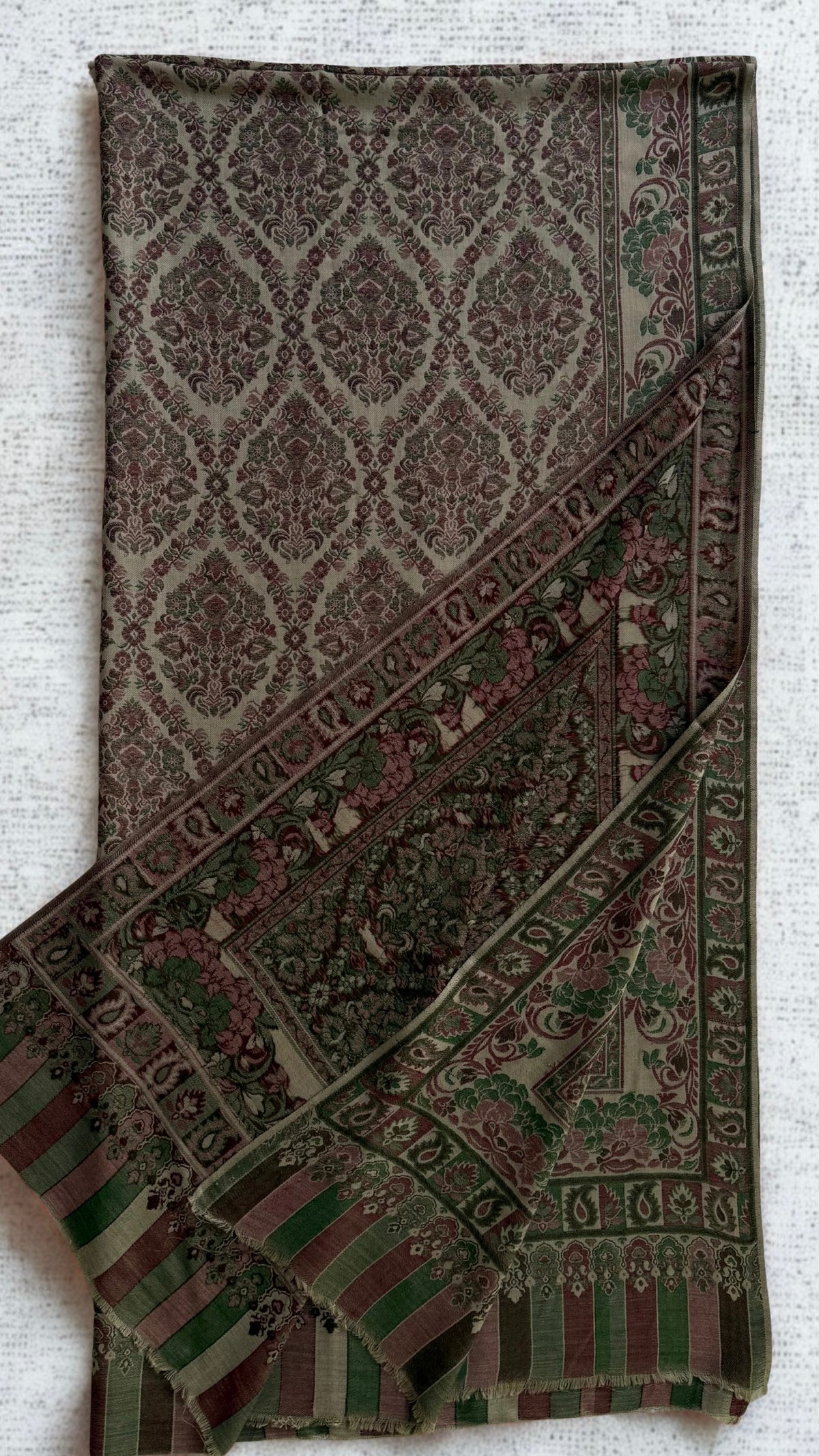 Plum and moss Kani pashmina shawl laid flat, all-over ogee medallion lattice with floral and paisley borders and an arcaded striped end panel
