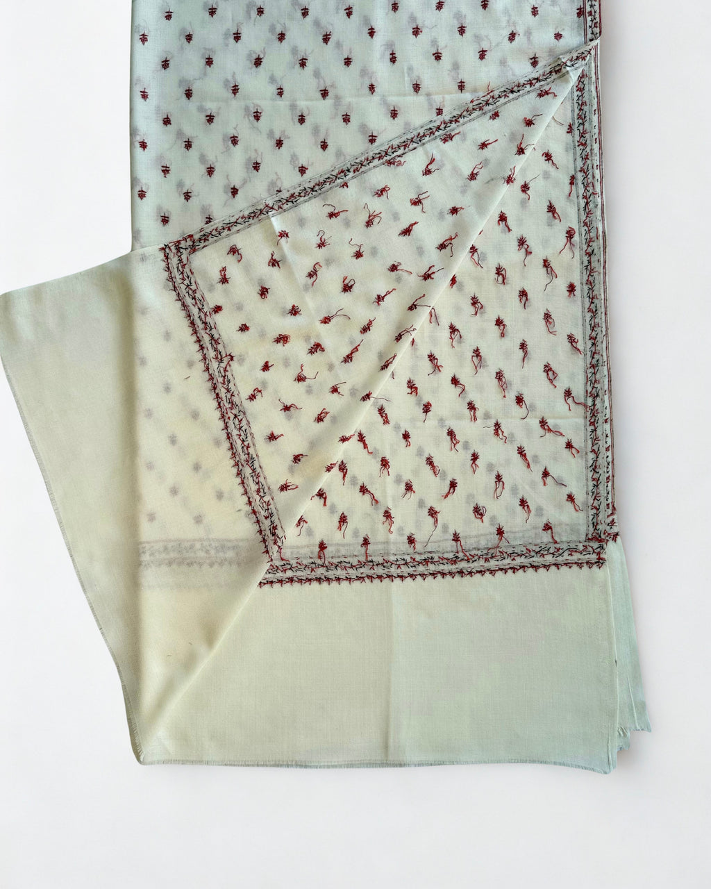 Ivory hand-embroidered pashmina shawl folded flat, crimson buti across the field with a floral border