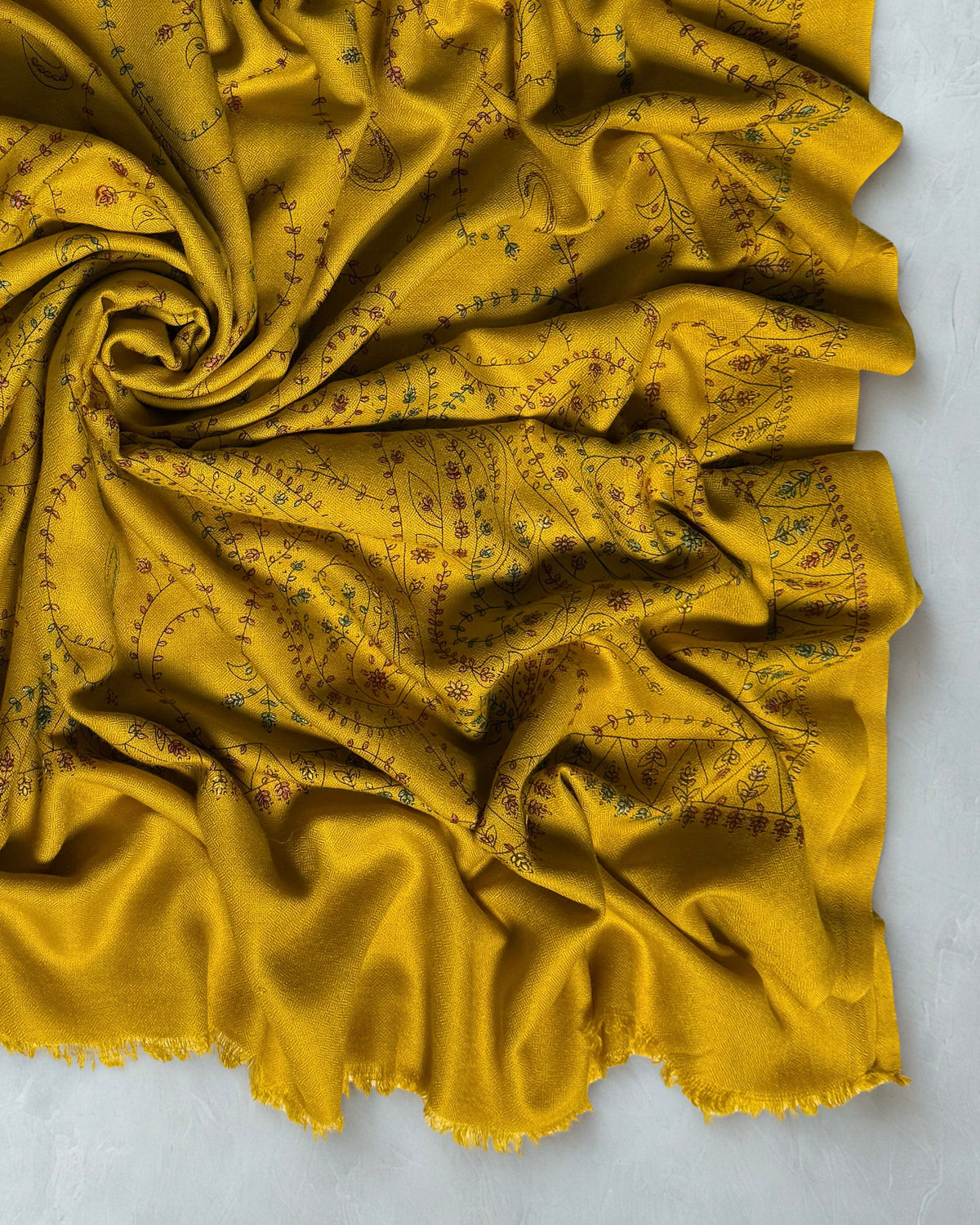Close-up of the fine hand embroidery and fringed edge on the mustard Swati Shahtoosh shawl