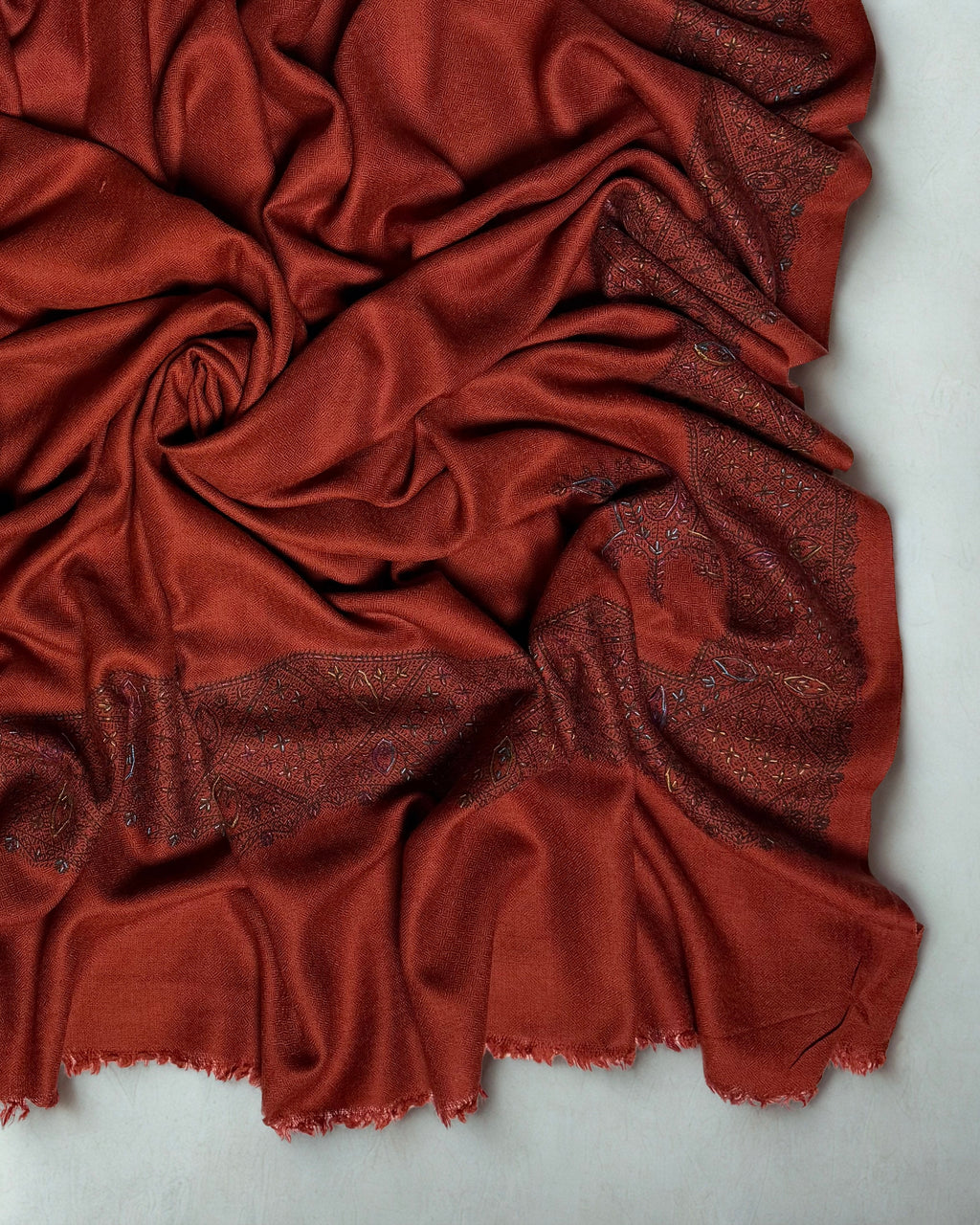 Rust Swati Shahtoosh shawl gathered in folds, the lattice border catching the light against the deep rust ground