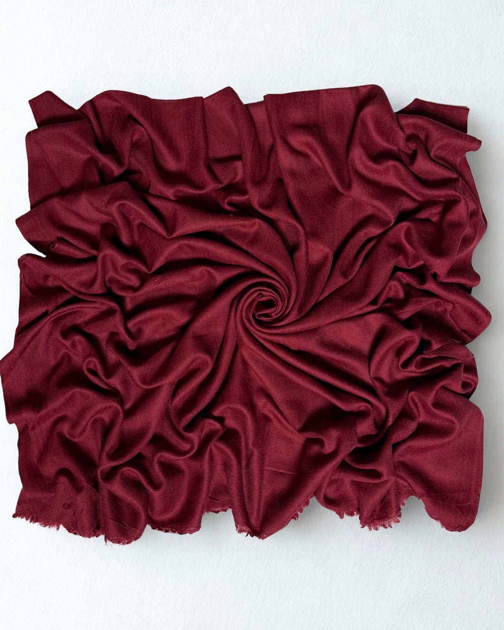 Maroon Swati Shahtoosh shawl gathered in a swirl, the deep wine-red cloth catching light along the folds