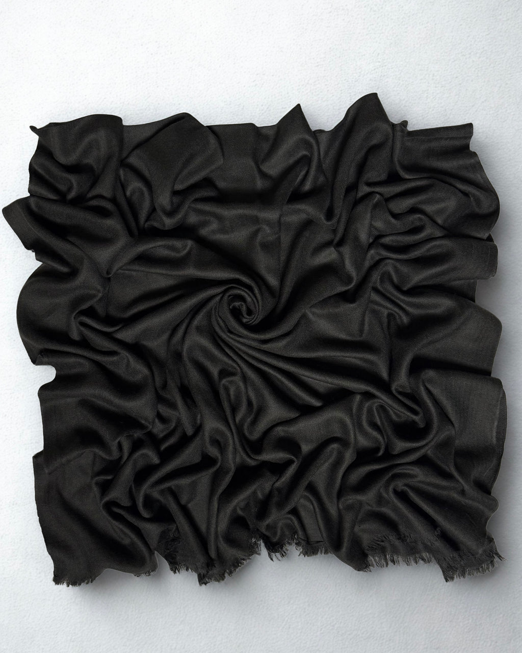 Charcoal black Swati Shahtoosh shawl gathered in a swirl, the soft matt cloth catching light along the folds