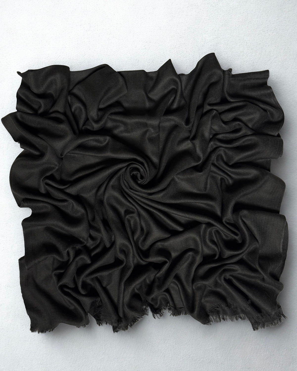 Charcoal black Swati Shahtoosh shawl gathered in a swirl, the soft matt cloth catching light along the folds