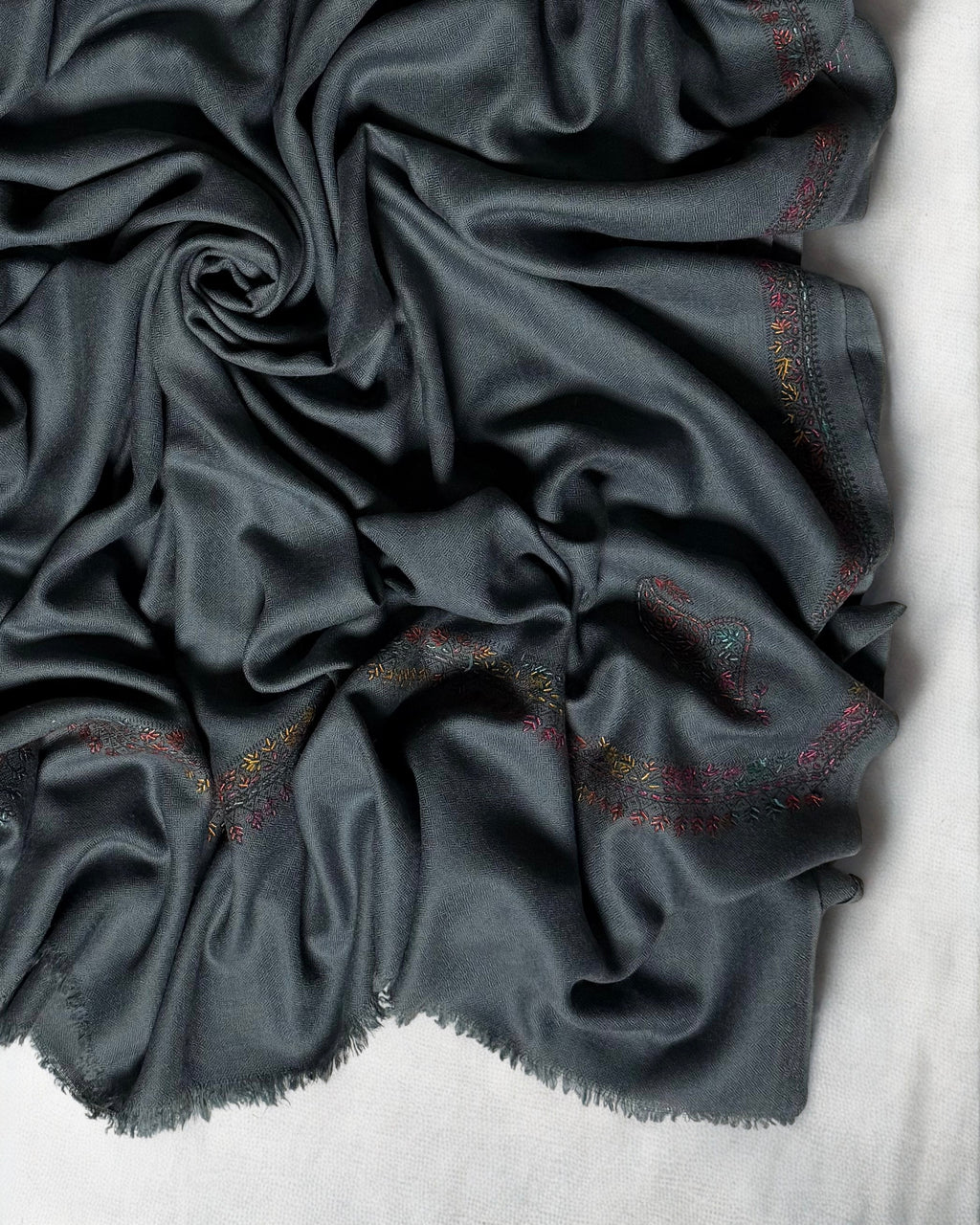 Close-up of the multicoloured hand-embroidered border and fringed edge on the slate grey Swati Shahtoosh shawl