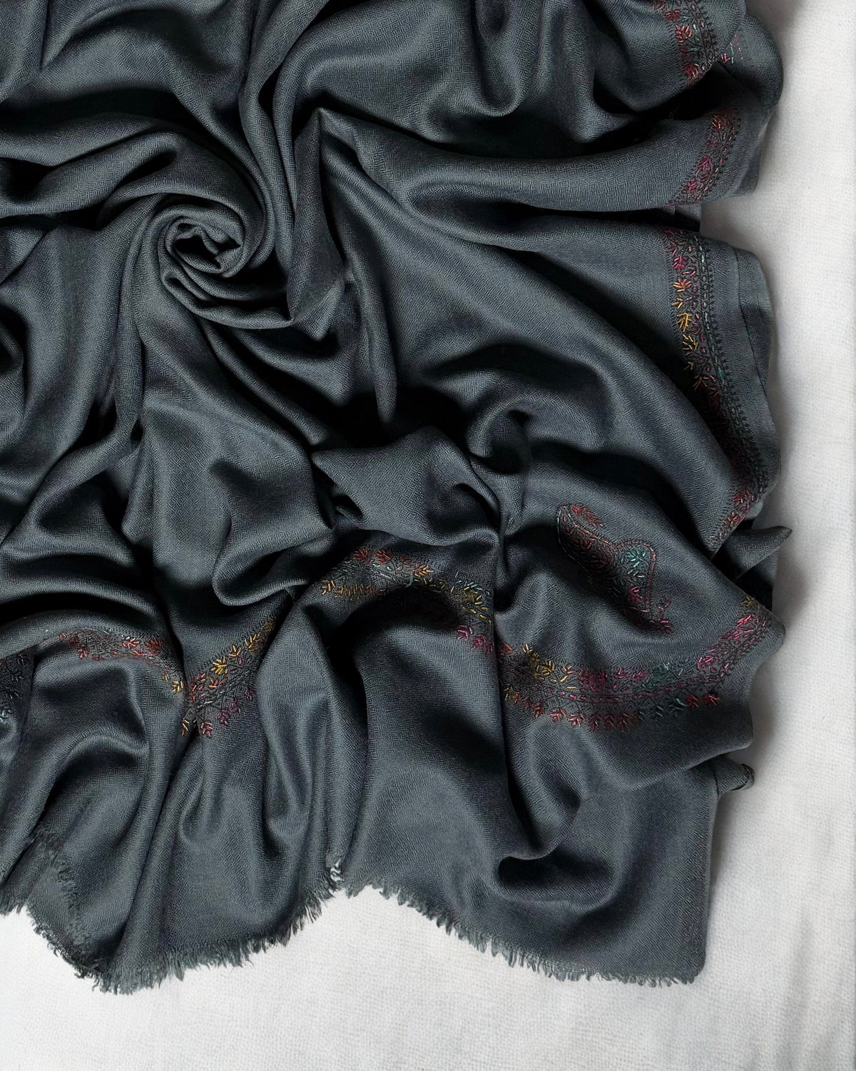 Close-up of the multicoloured hand-embroidered border and fringed edge on the slate grey Swati Shahtoosh shawl