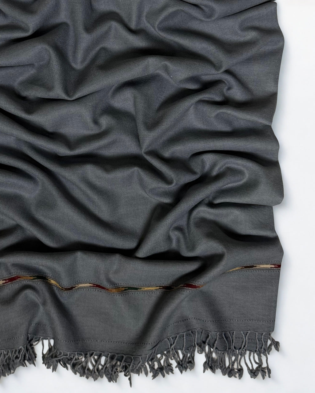 Close-up of the grey men's Swati pashmina shawl showing the multicoloured woven band and knotted fringe