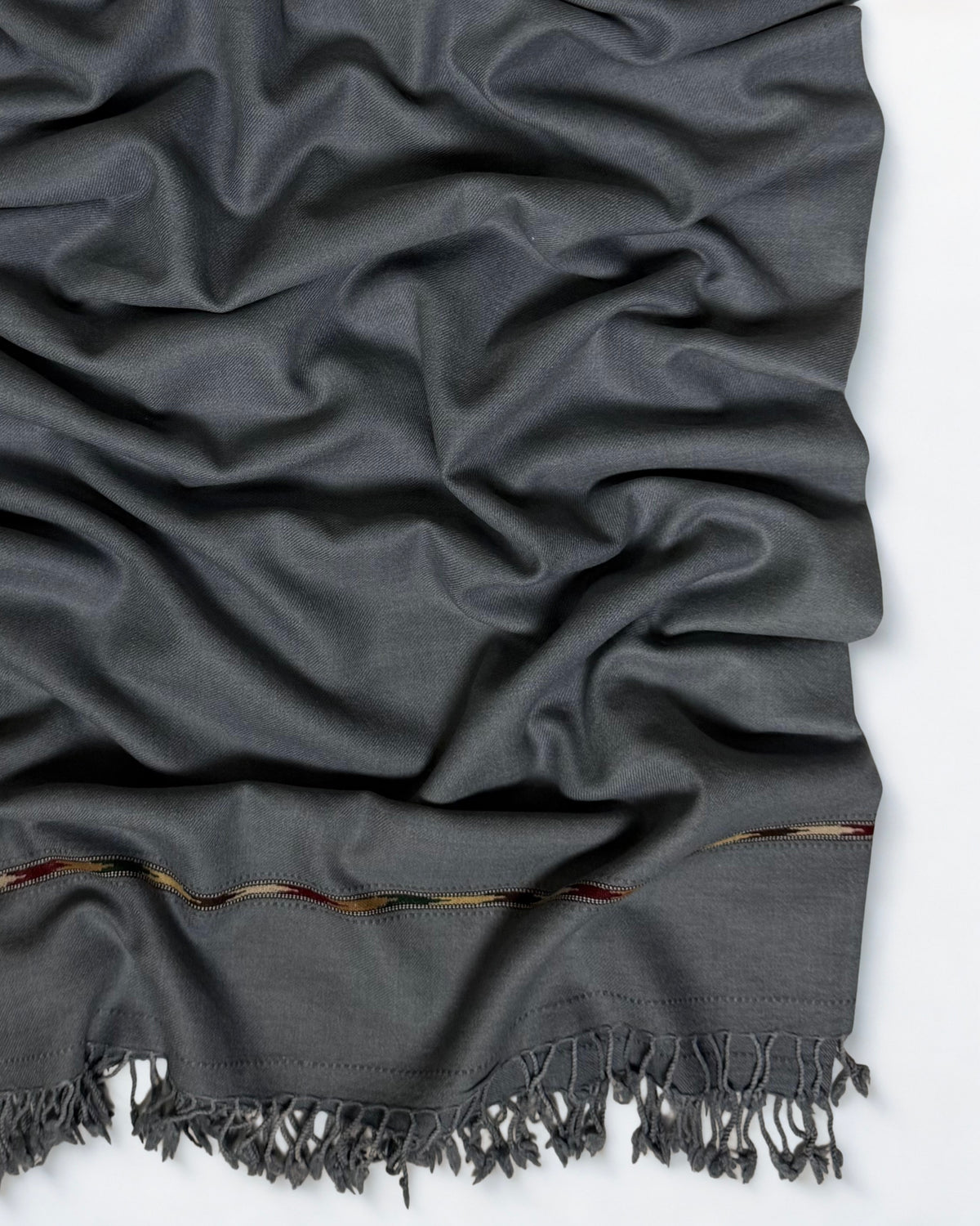 Close-up of the grey men's Swati pashmina shawl showing the multicoloured woven band and knotted fringe