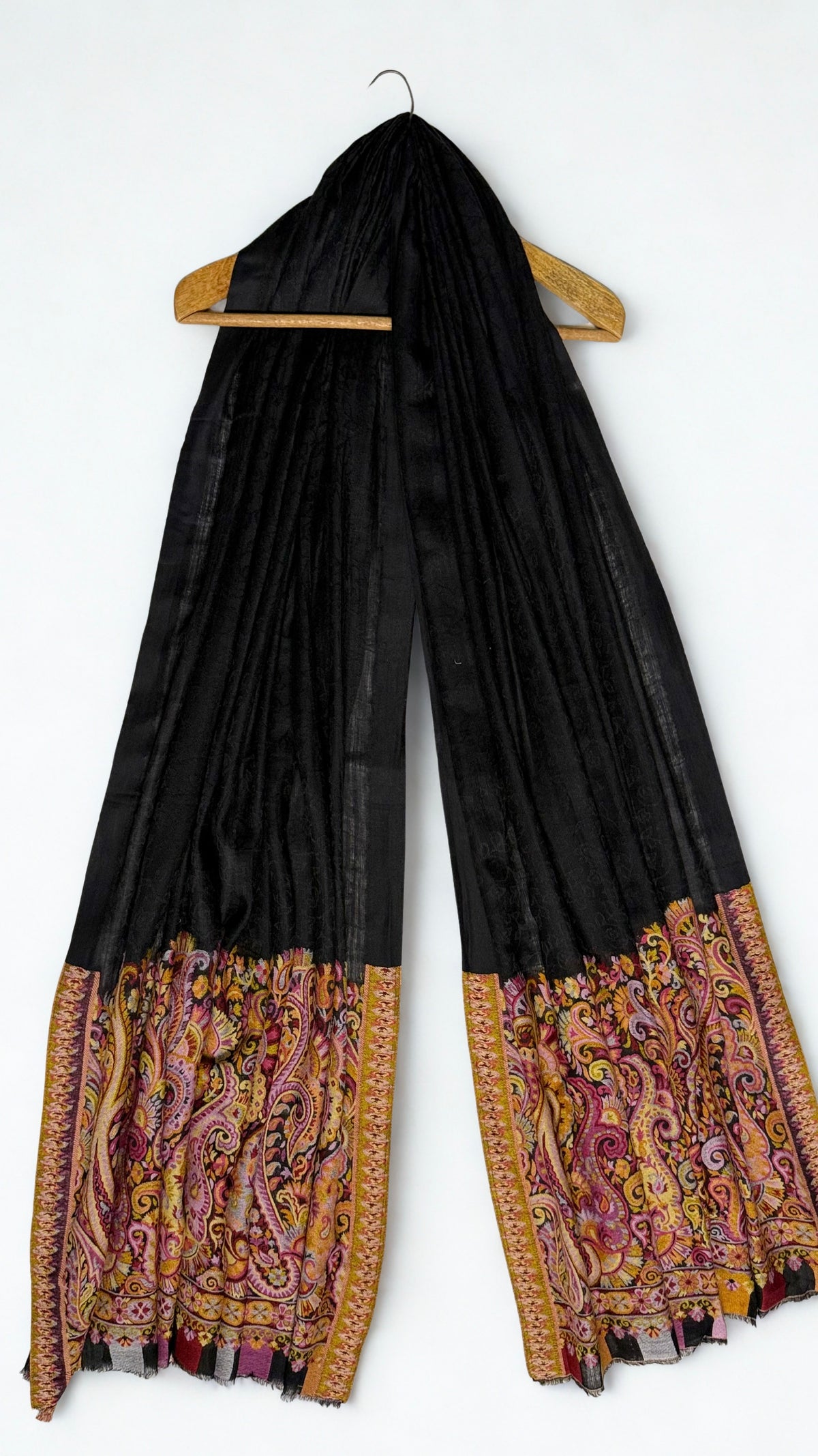 Black ek rukh pashmina ring shawl on a wooden hanger, falling in long pleats to the patterned ends