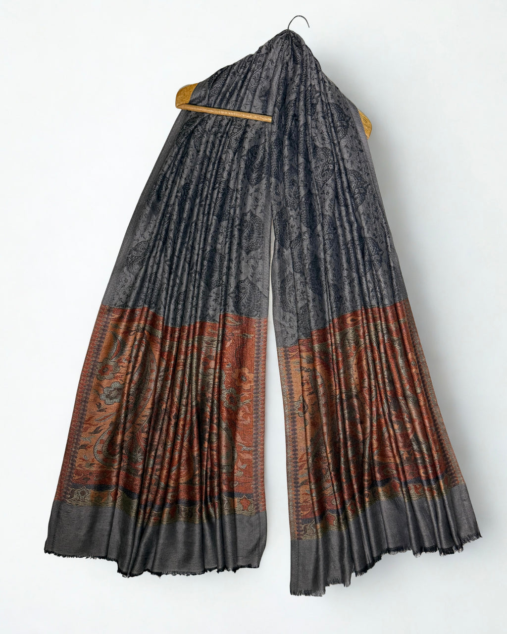 Charcoal Palladar shawl hanging from a wooden hanger, dark paisley field above and rust paisley pallas at both ends