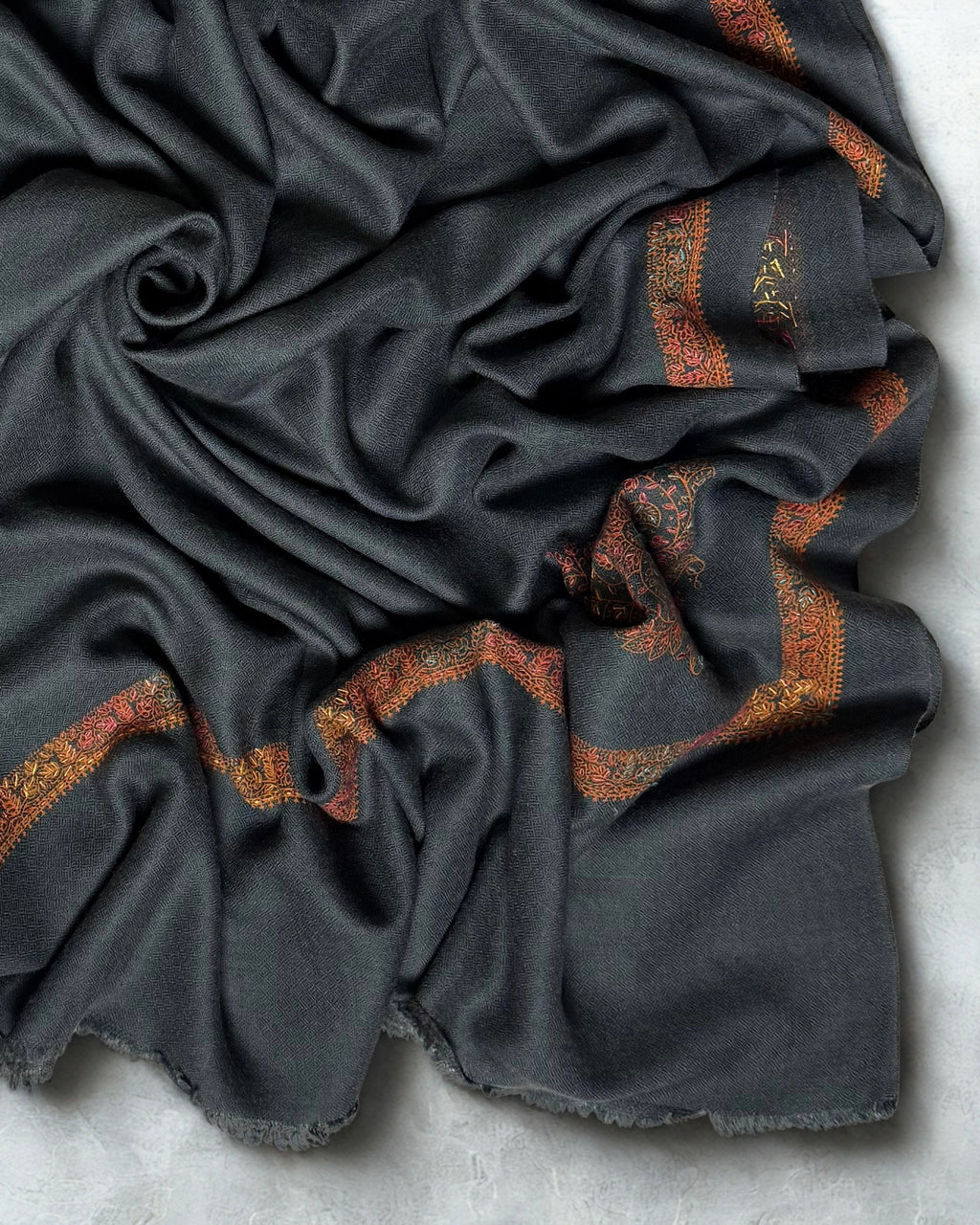 Close-up of the rust hand-embroidered border and fringed edge on the charcoal Swati Shahtoosh shawl
