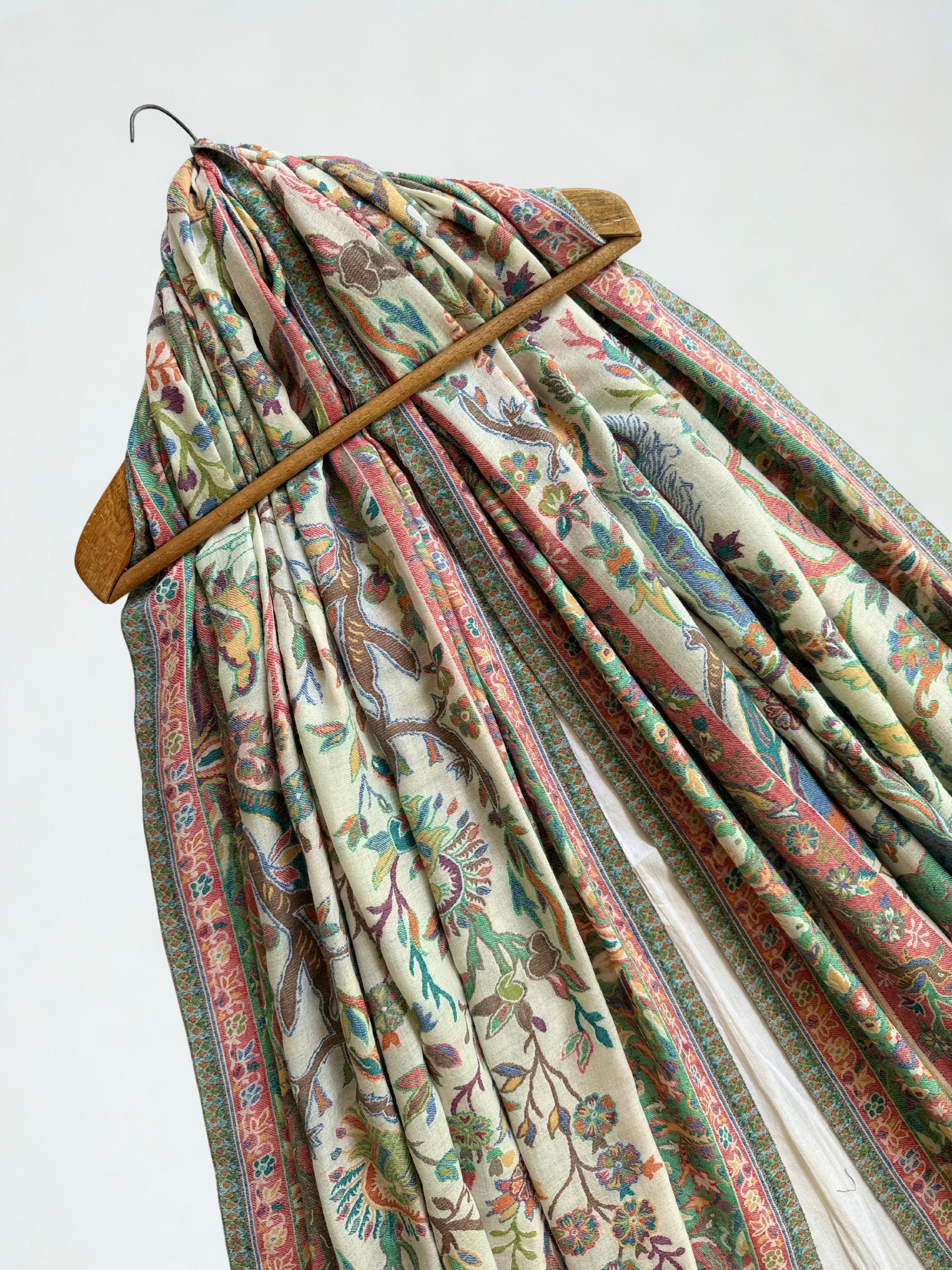 Ivory Kani shikargah pashmina shawl on a wooden hanger, falling in long pleats to show its full length and striped ends