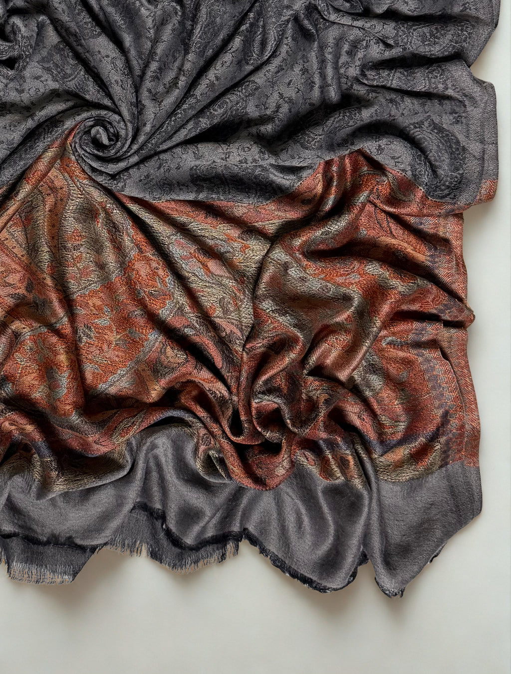 Close-up of a charcoal Palladar shawl swirled to show the black paisley field meeting the rust paisley pallu and plain fringed end