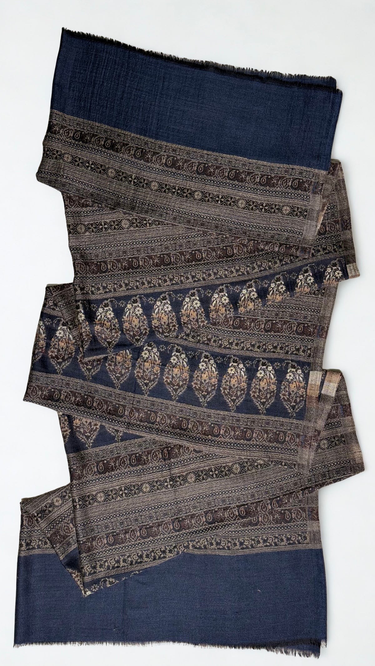 Indigo and bronze Indian pashmina shawl on a wooden hanger, falling in fine pleats to show its full length and indigo borders