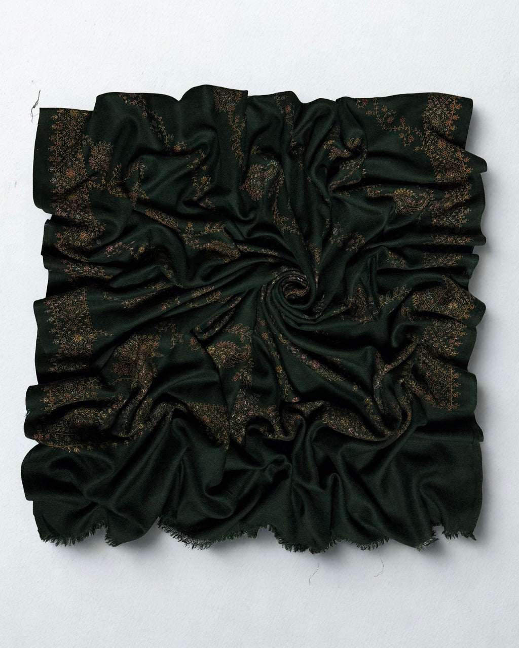 Deep forest green hand-embroidered Swati Shahtoosh shawl swirled from above, showing the embroidered border and fringed edges