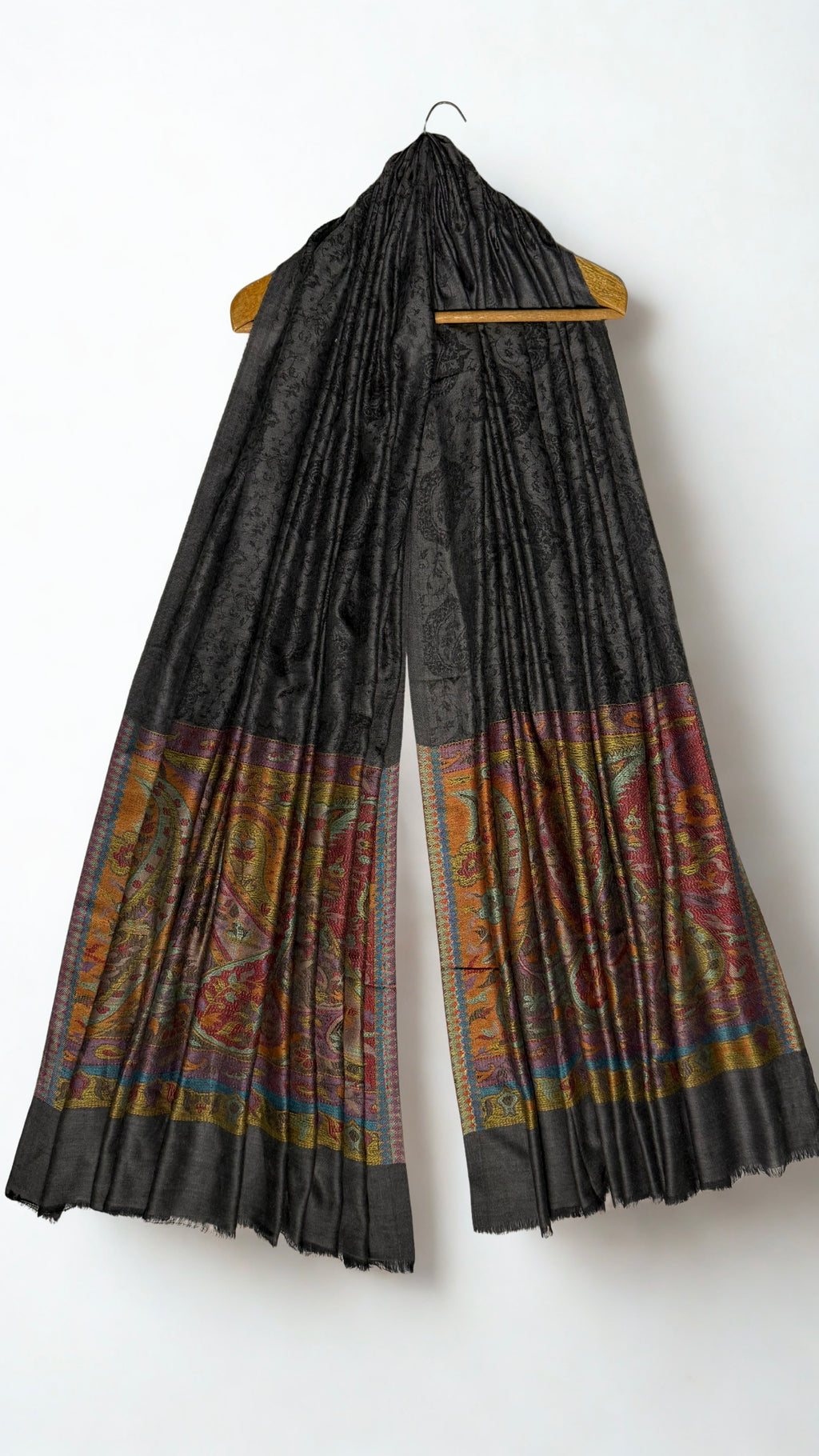 Dark charcoal Palladar shawl hanging from a wooden hanger, with saffron and crimson paisley pallas at both ends