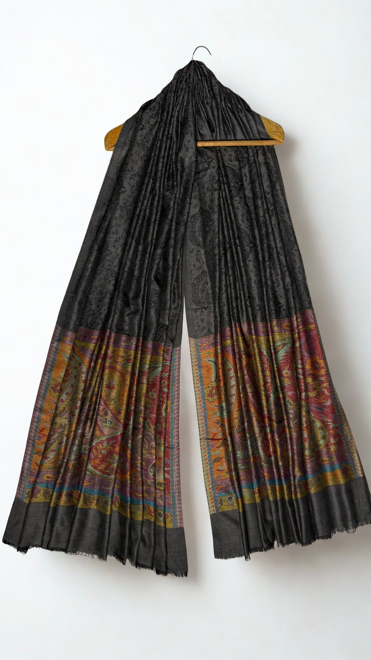 Dark charcoal Palladar shawl hanging from a wooden hanger, with saffron and crimson paisley pallas at both ends