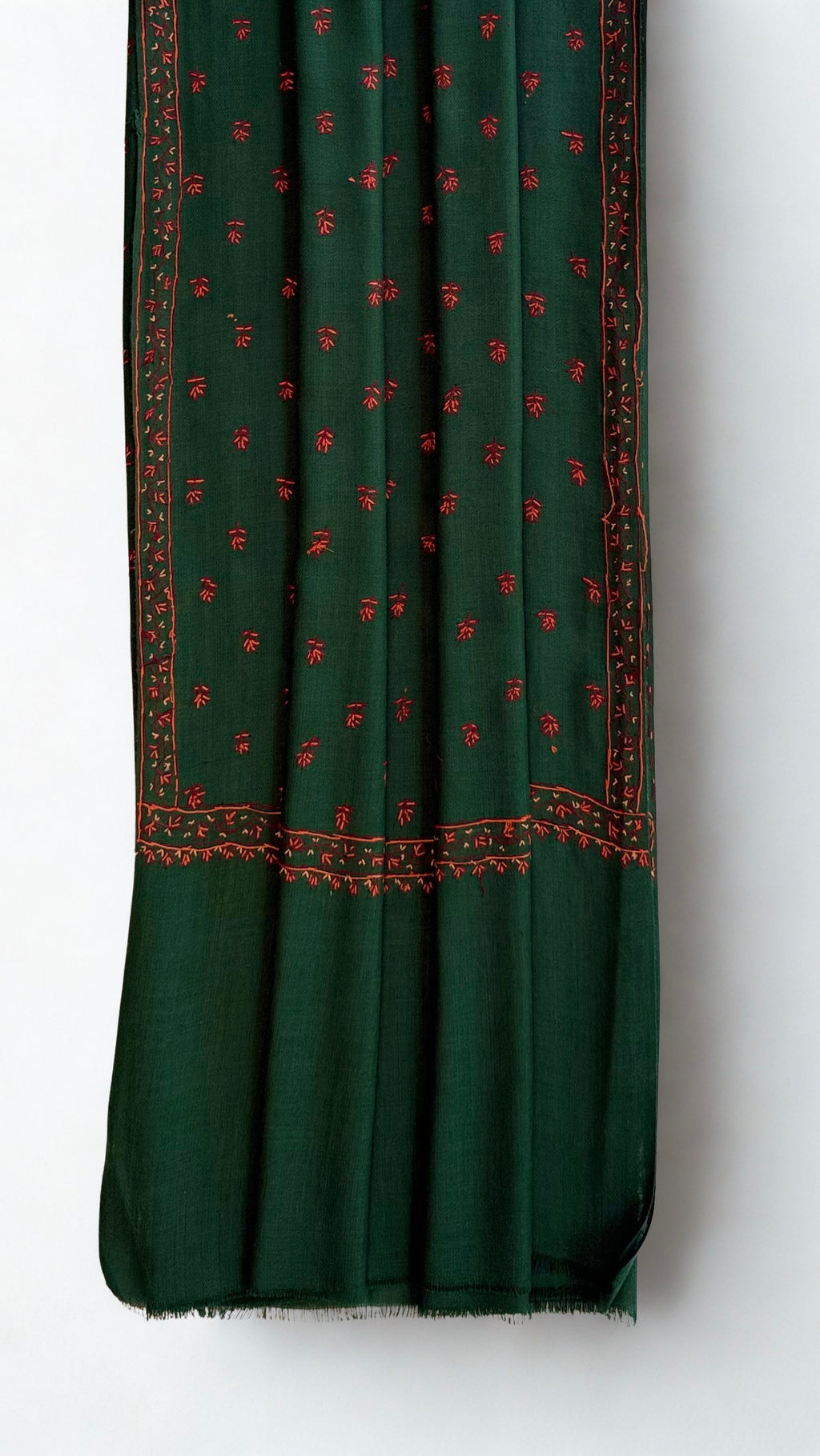 Corner of an emerald pashmina shawl folded back to show the crimson hand embroidery and reverse thread-work