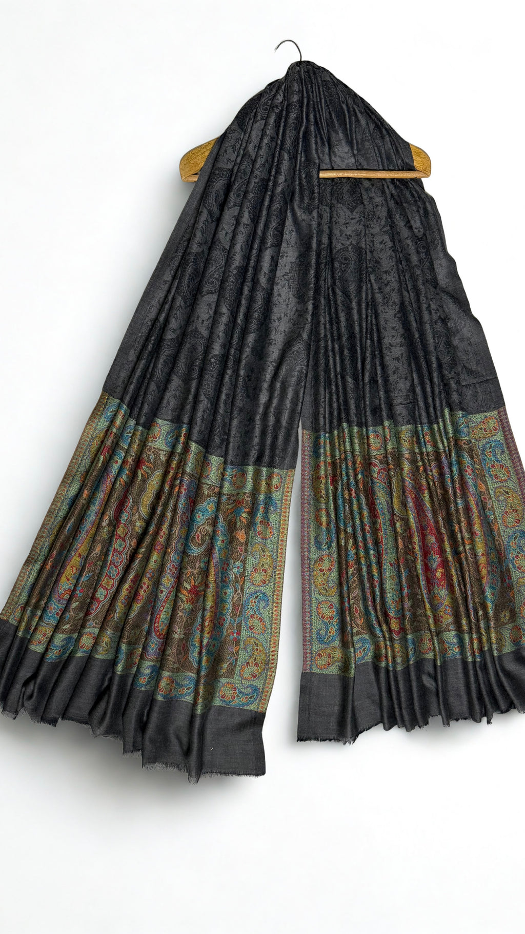 Dark charcoal Palladar shawl hanging from a wooden hanger, with jewel-tone paisley pallas at both ends