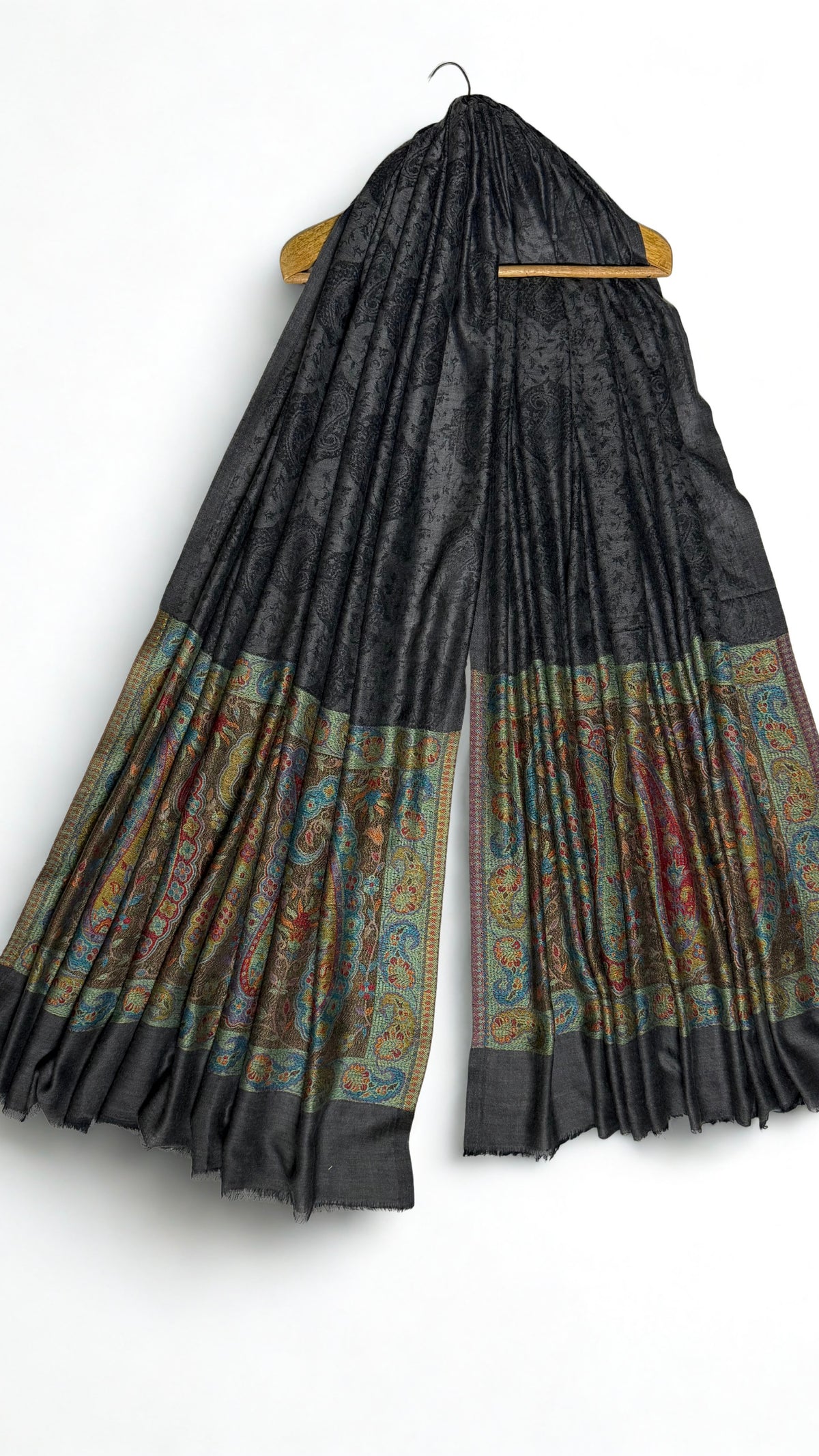 Dark charcoal Palladar shawl hanging from a wooden hanger, with jewel-tone paisley pallas at both ends
