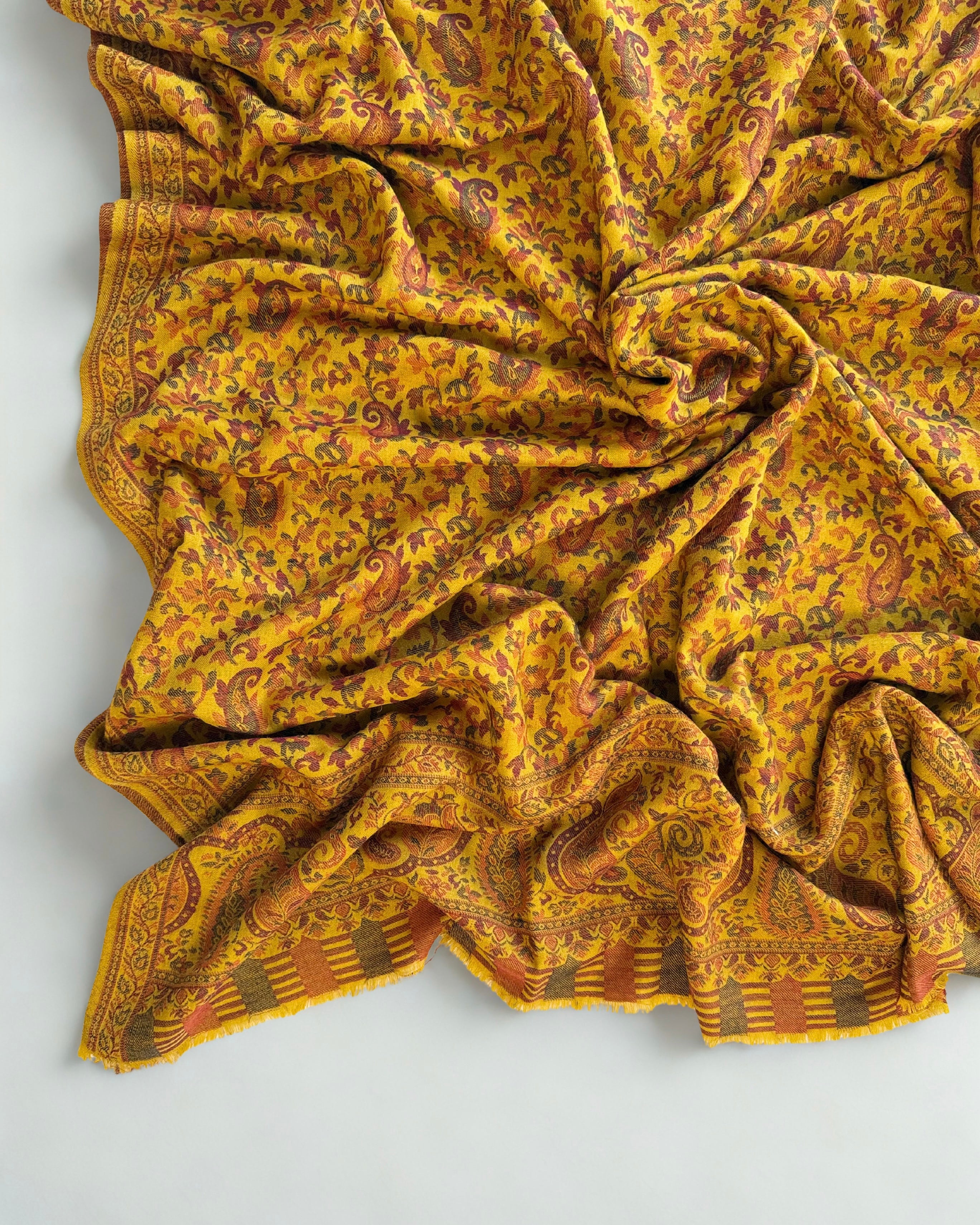 Mustard Kani pashmina shawl folded to show the broad woven end border in rust and moss green
