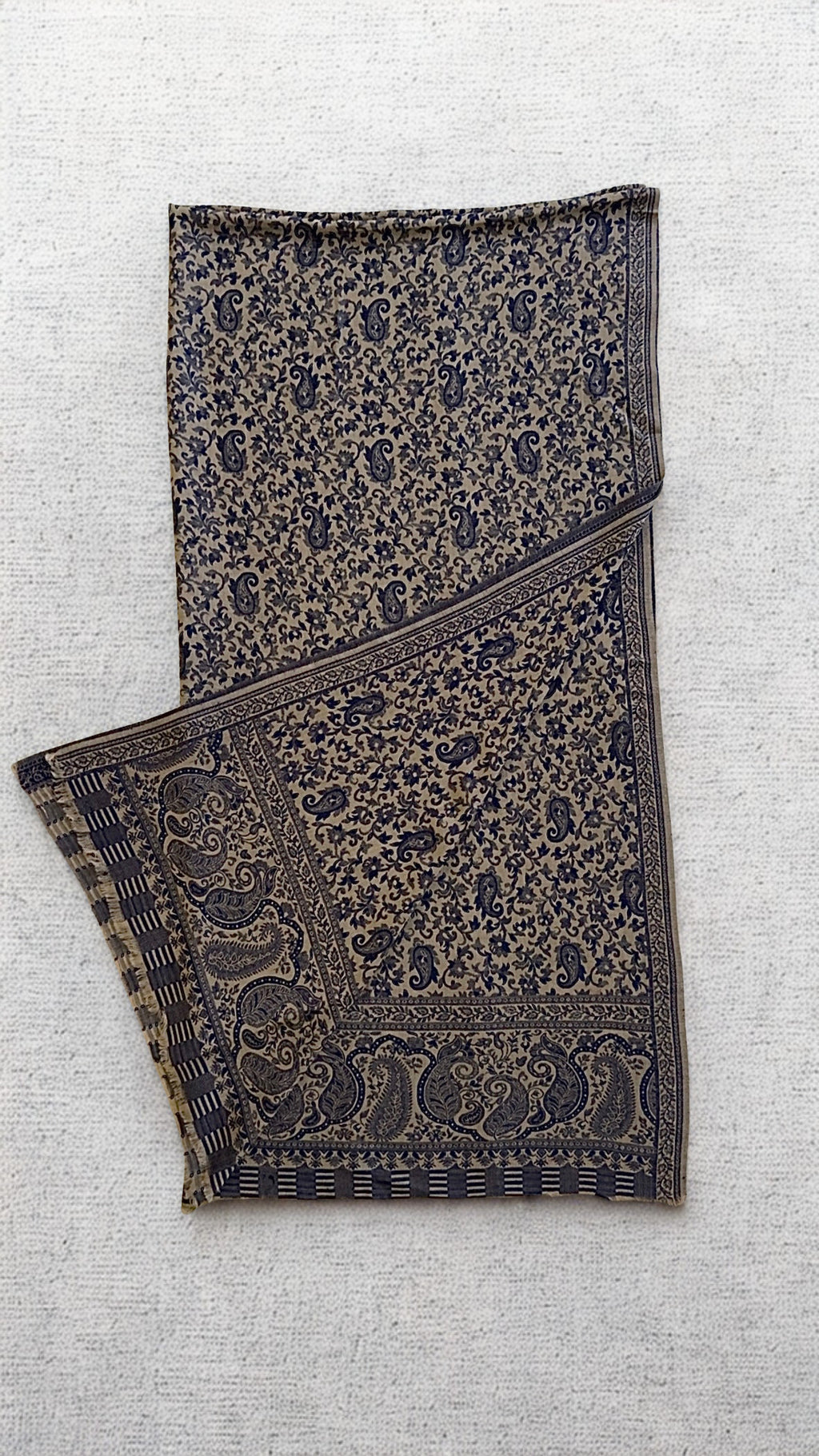 Stone-grey Kani pashmina shawl laid flat, fine navy paisley across the field with a deep ornamented end border