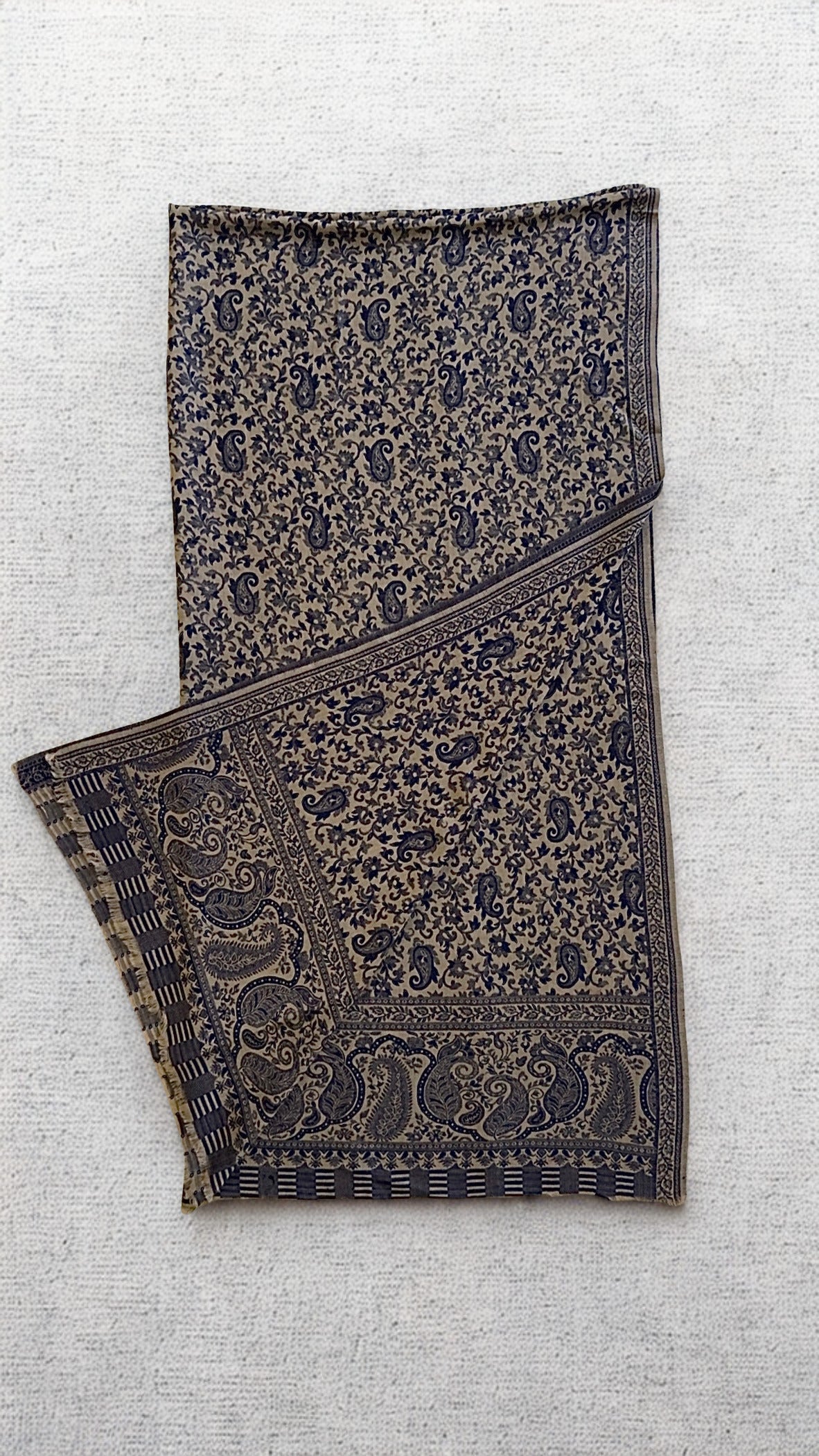 Stone-grey Kani pashmina shawl laid flat, fine navy paisley across the field with a deep ornamented end border