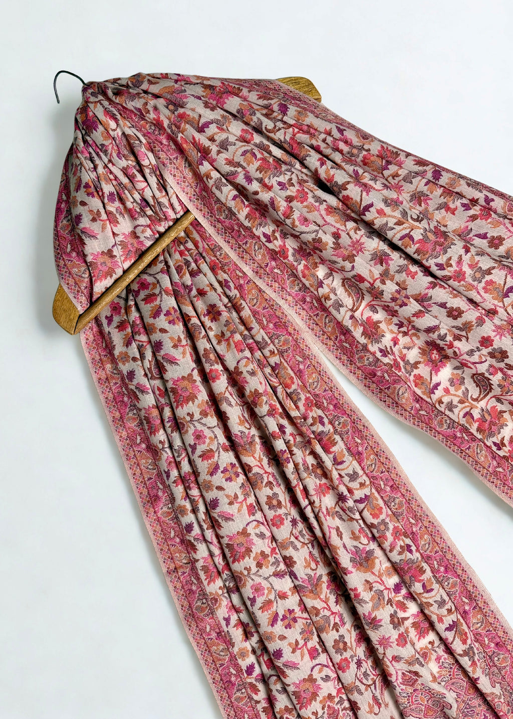 Rose and oyster Kani pashmina shawl hung on a hanger, showing its full length and drape