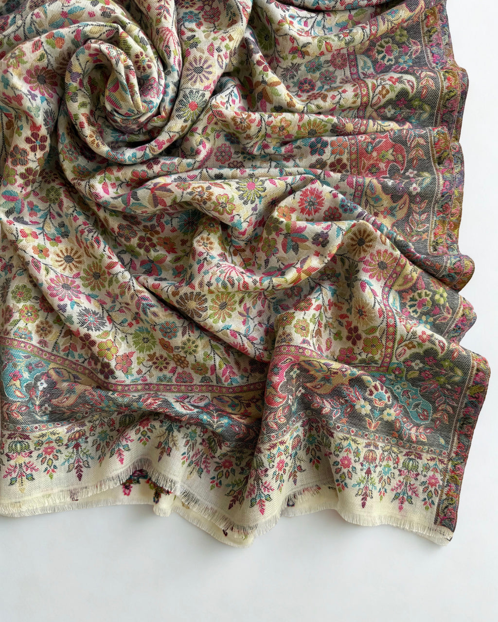 Close view of the small rose, teal and olive flowers woven with gold zari on an ivory pashmina ground