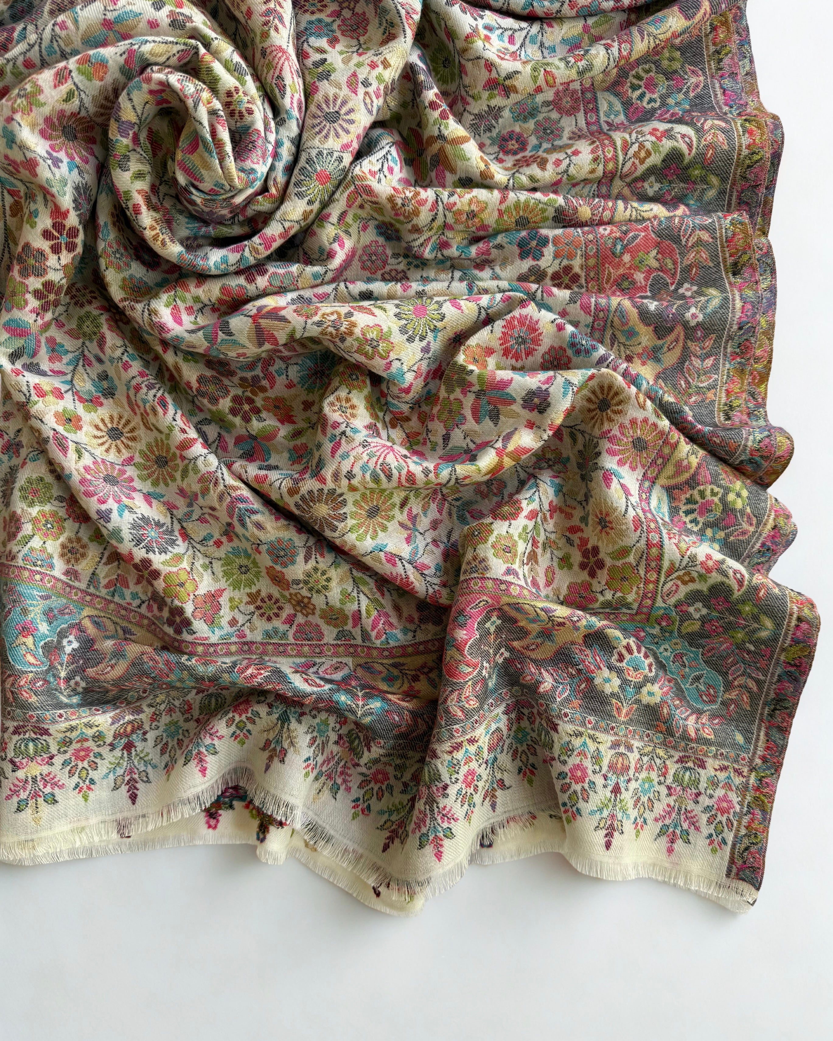 Close view of the small rose, teal and olive flowers woven with gold zari on an ivory pashmina ground