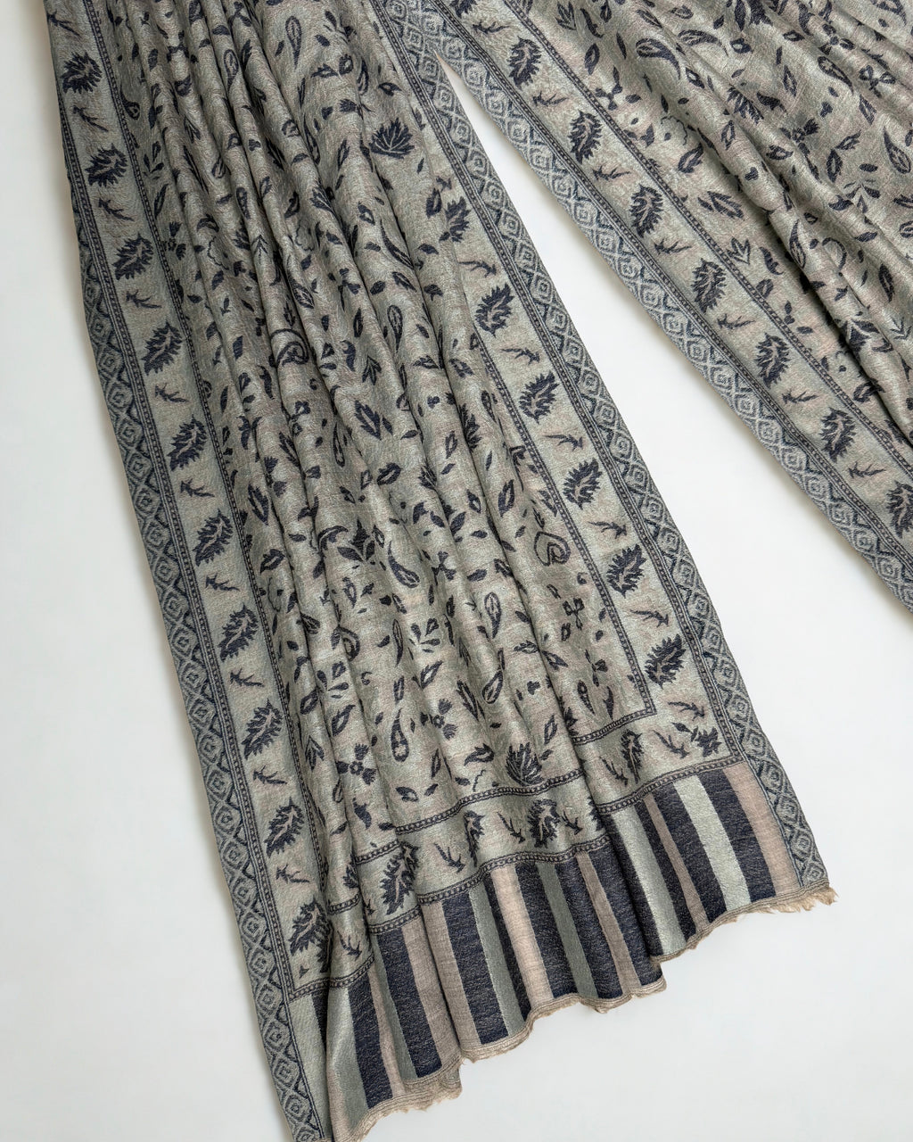 Stone and indigo Indian pashmina shawl gathered over a hanger, showing the drape and the woven leaf border
