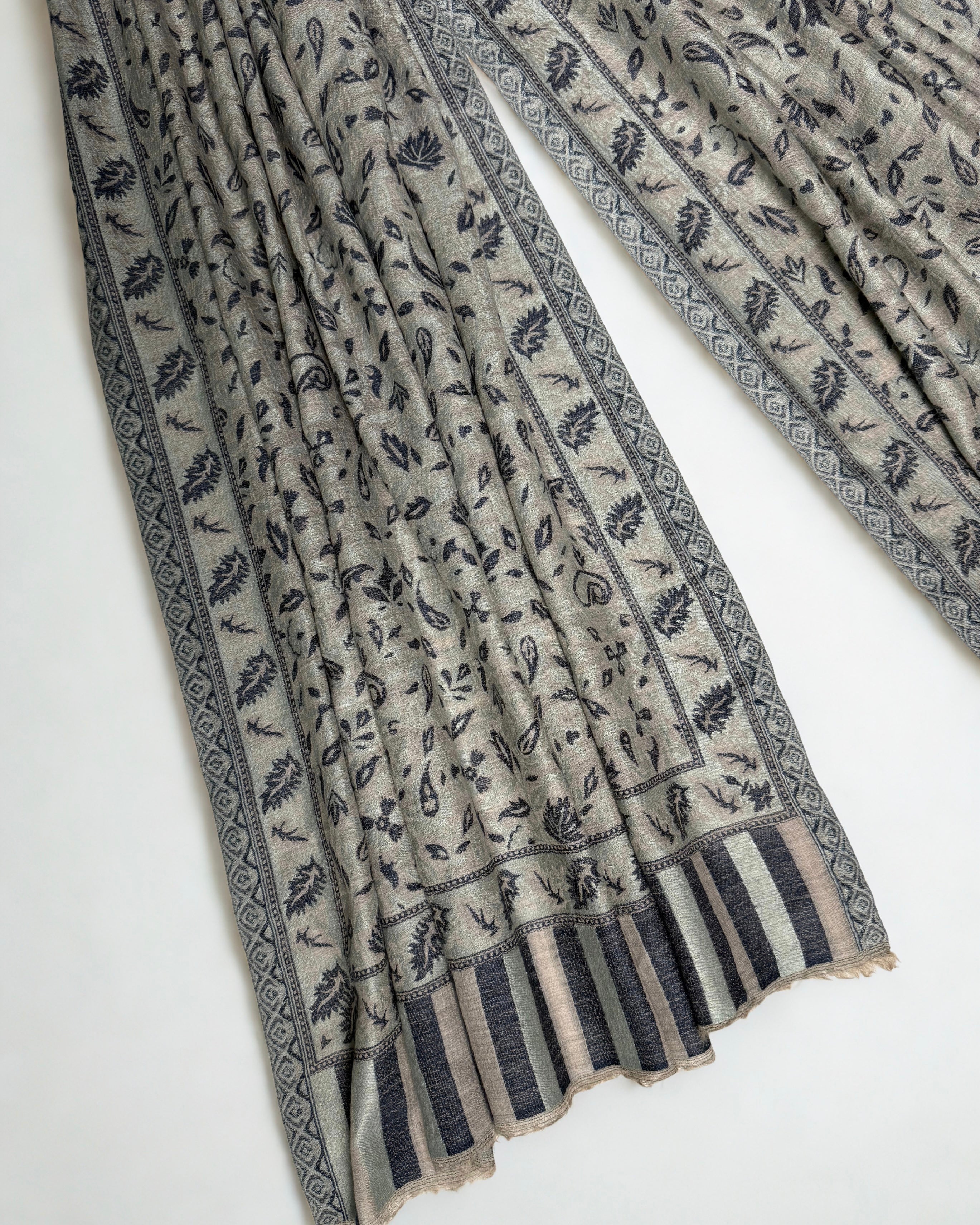 Stone and indigo Indian pashmina shawl gathered over a hanger, showing the drape and the woven leaf border