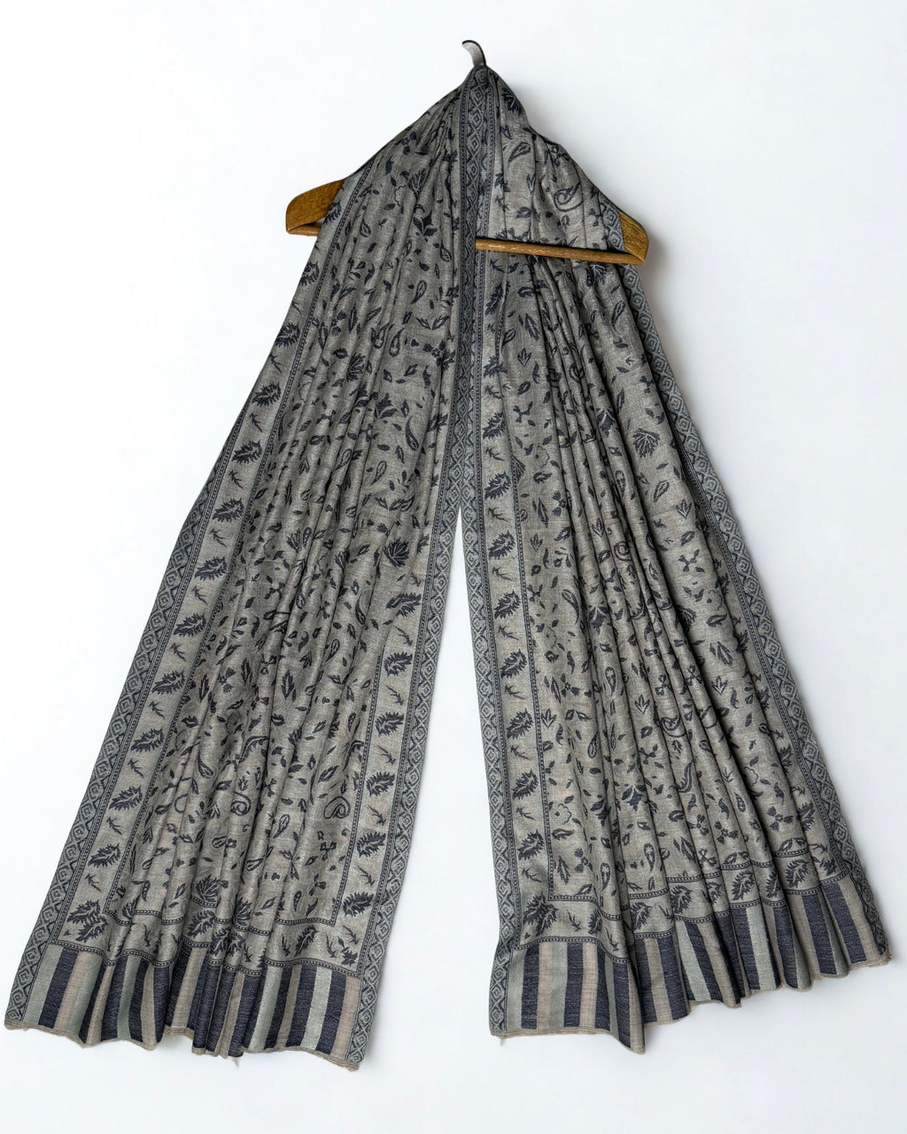 Stone and indigo Indian pashmina shawl on a wooden hanger, falling in fine pleats to show its full length and striped ends